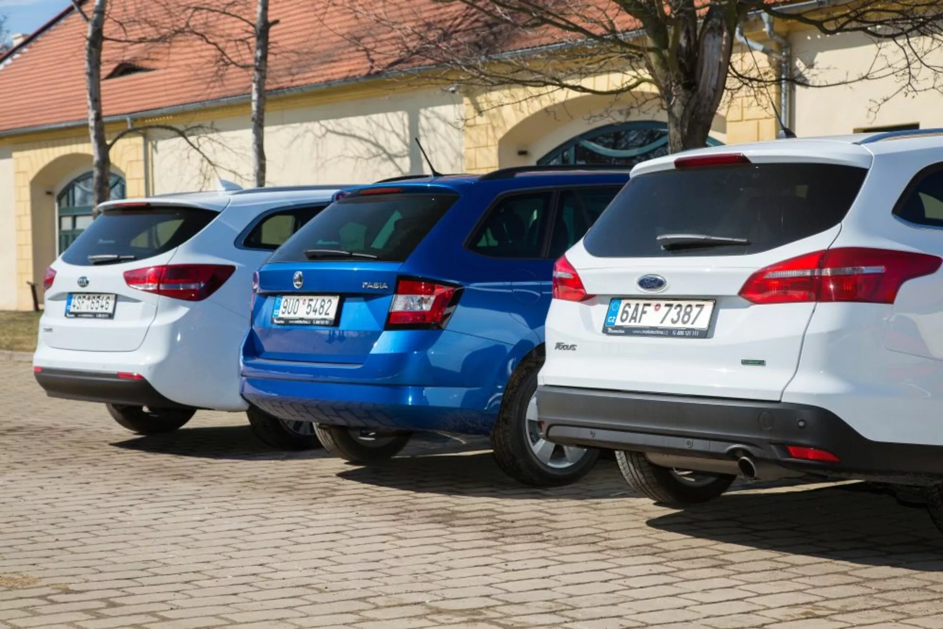 Razvrstitev treh kombilimuzin, vključno z belim Ford Focusom letnik 2011, parkiranih pravokotno z zadnjimi konci obrnjenimi proti kameri, prikazujemo zadnje luči in značilnosti dizajna zadnjega dela na dobro osvetljenem parkirišču.