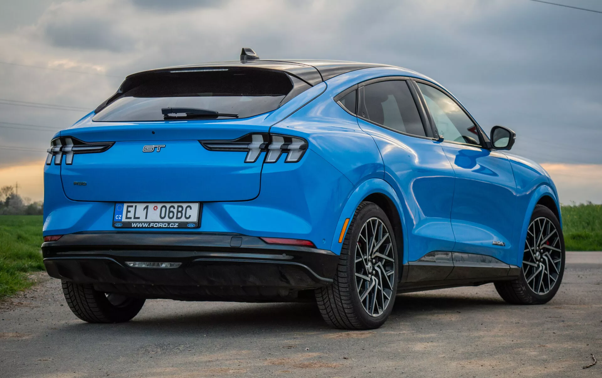 Modri električni SUV Ford Mustang Mach-E 2020 prikazan iz perspektive tri četrtine zadaj, poudarja njegov eleganten aerodinamičen dizajn, sodobne zadnje LED luči, večkraka lita platišča, oznako električnega vozila in tehnološke lastnosti
