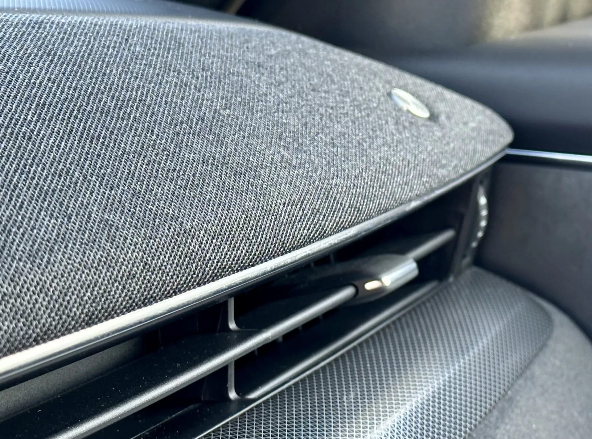 Detajlen pogled v notranjosti Ford Mustang Mach-E 2020, ki prikazuje del armaturne plošče ali vratnega panela z vgrajeno vrhunsko tkanino zvočnika, emblema, ki nakazuje partnerstvo z proizvajalcem avdio opreme visokega razreda, ob tem pa sijoč črn prezračevalnik