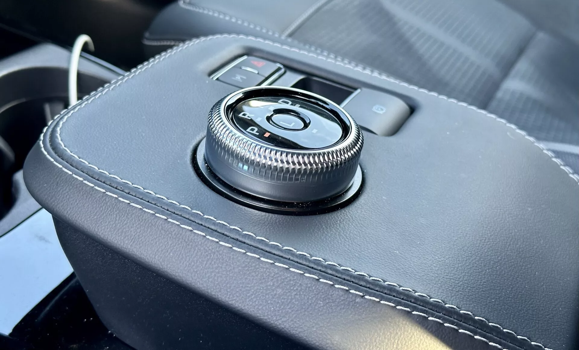 Podroben pogled na notranjost Ford Mustang Mach-E 2020 z rotacijskim gumbom na centralni konzoli na usnjeno površino z belimi šivi, ki zagotavlja ergonomski vmesnik za informacijsko-zabavni sistem