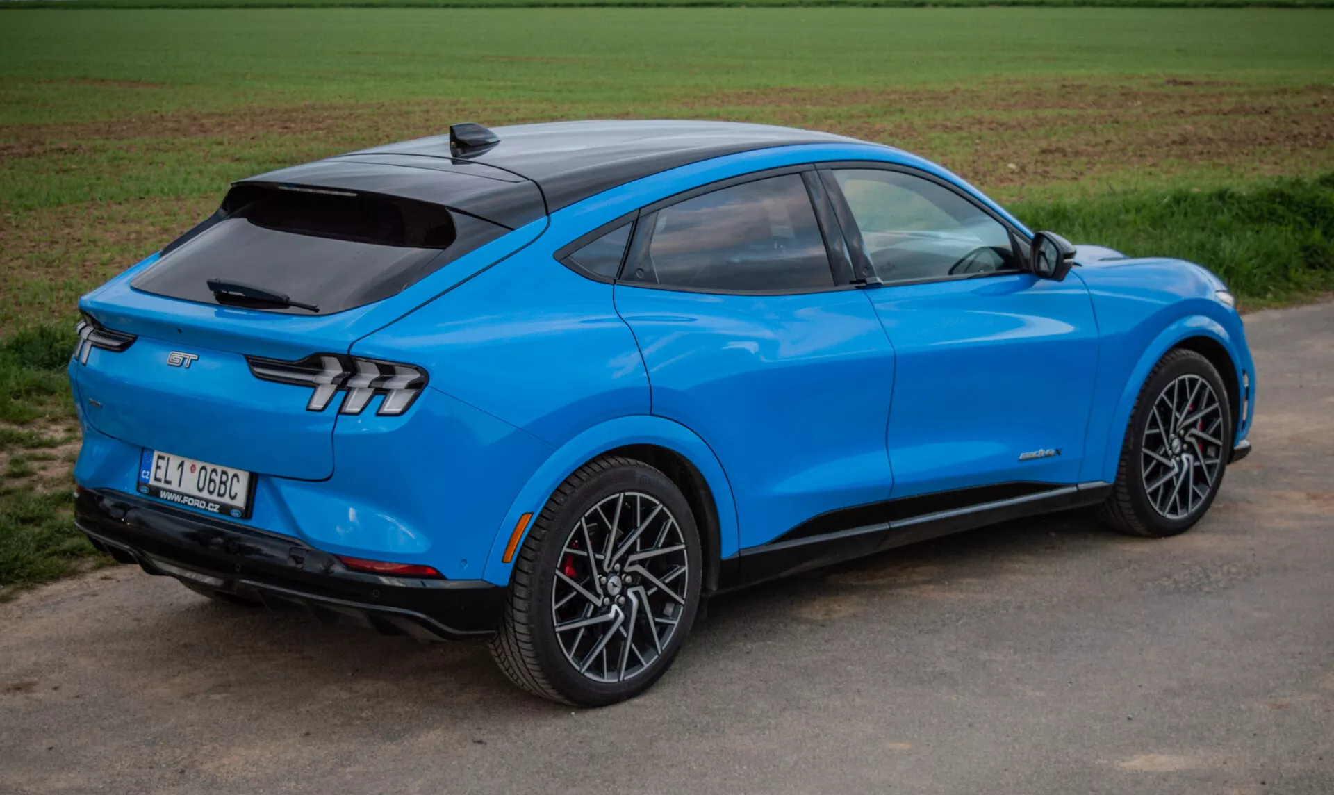 Svetlo modri električni SUV Ford Mustang Mach-E 2020 v dinamičnem pogledu s treh četrtin zadaj, ki poudarja aerodinamično oblikovanje, elegantne zadnje luči in športna zlitinska kolesa, kar prikazuje napredno tehnologijo in električni pogon.