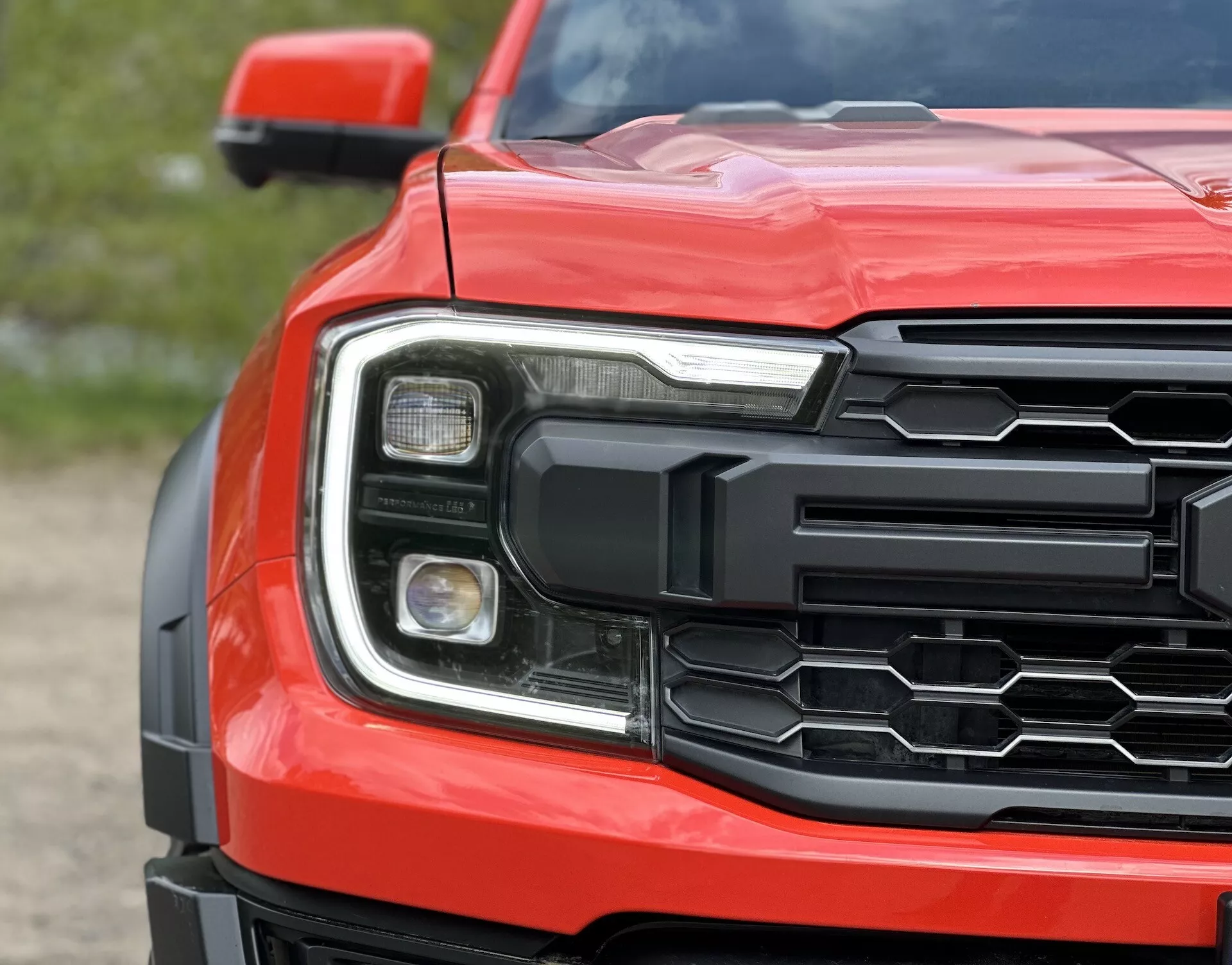 Podroben pogled na sprednji kot Ford Rangerja 2022 s šestkotno masko, podrobnim sklopom žarometov in oblikovanim pokrovom motorja v rdeči barvi