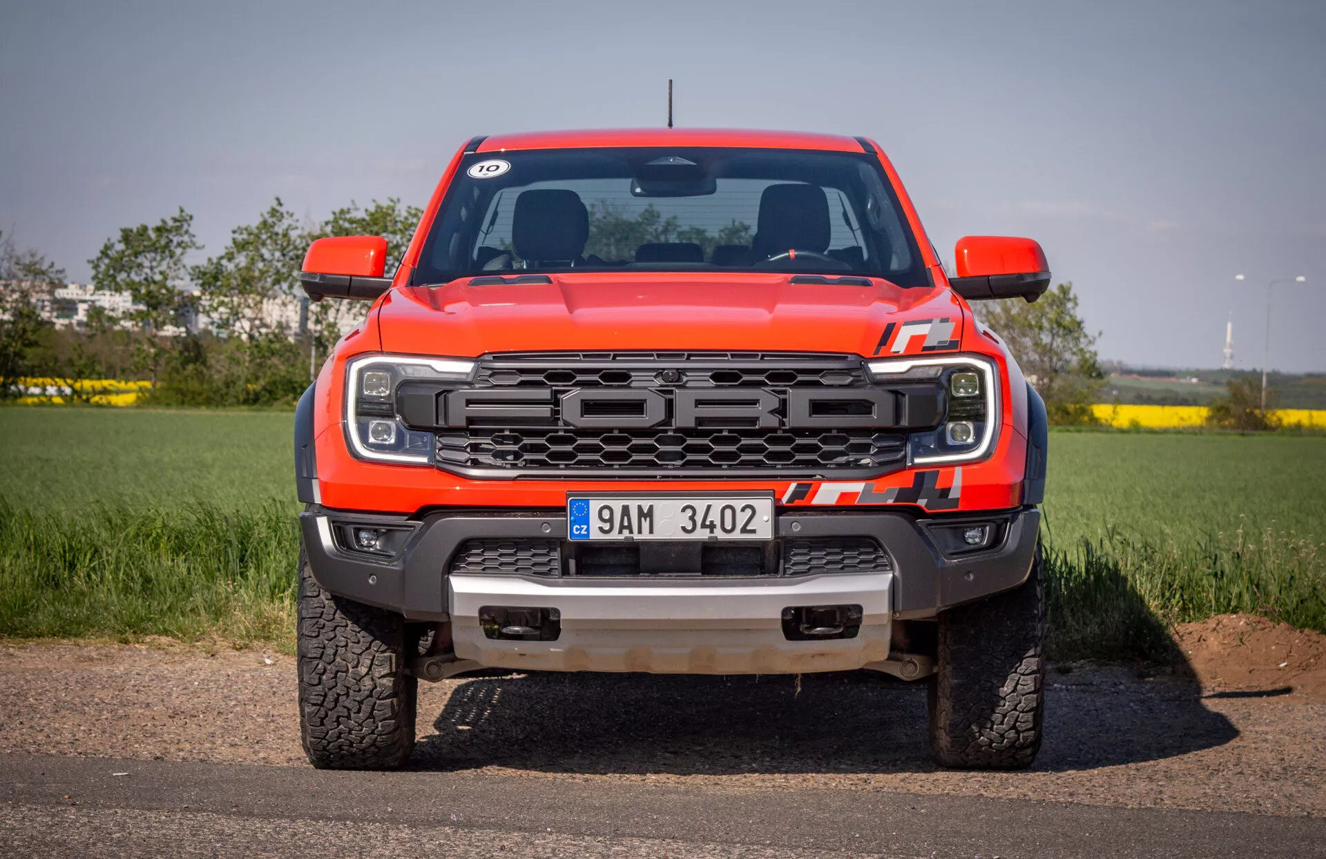 Sprednji pogled na rdeči pickup Ford Ranger 2022 na asfaltu z ozadjem čistega neba, z značilnostmi rešetke, LED žarometi, sprednjim odbijačem z vlečnimi kljukami in zaščitno ploščo ter logotipom Ford