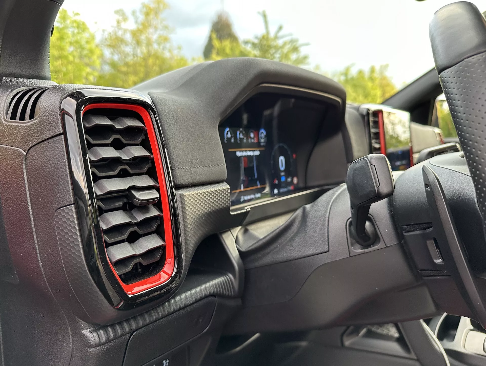 Pogled na notranjost Ford Rangerja 2022 iz perspektive voznika, prikazuje digitalno instrumentno ploščo in levo zračno rešetko z rdečim poudarkom, z rahlo izcentričnim kotom proti volanu, kar sugerira zavijanje