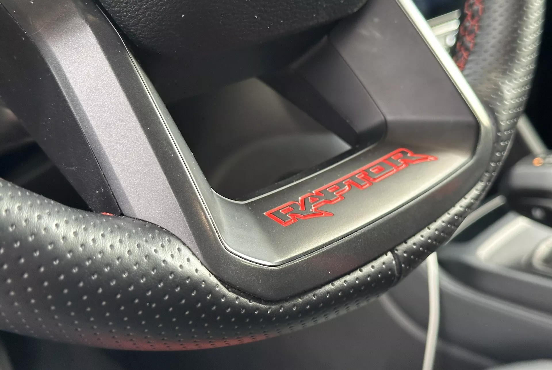 Posnetek iz bližine volana Dodge Viper, ki prikazuje perforirano usnje z rdečim šivom in značko 'Viper', kar kaže na športno, luksuzno notranjost avtomobila.