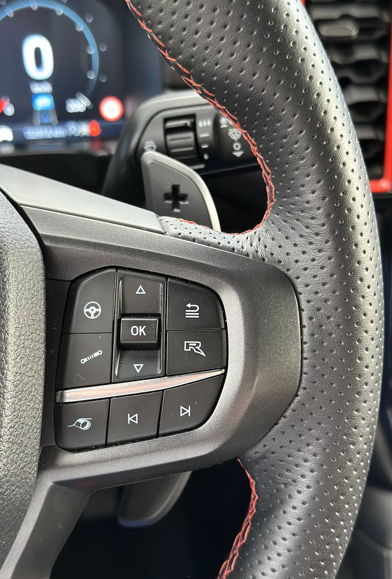 Približek volana Ford Ranger 2022 s poudarkom na gumbih in značilnostih leve strani, vključno z perforiranim usnjem z rdečimi šivi, iz perspektive voznika v pokončni orientaciji