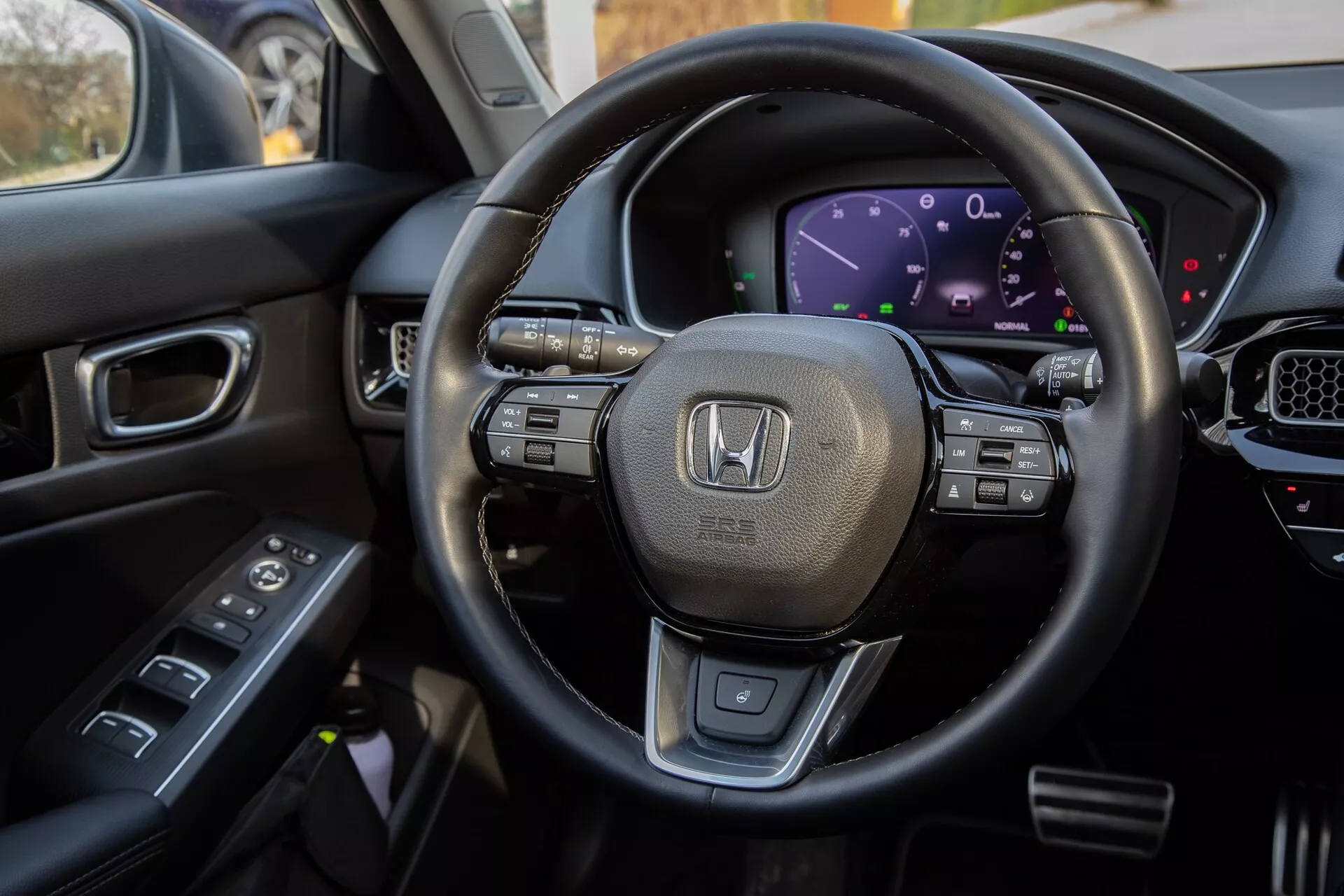 Notranji pogled na Honda Civic 2022 iz voznikovega sedeža, ki poudarja volan, oblečen v usnje z multifunkcijskimi kontrolami, digitalno armaturno ploščo, del sredinske konzole z zaslonom na dotik in kontrole na voznikovih vratih za celovit prikaz sodobnih tehnoloških funkcij in razkošnega oblikovanja vozila.