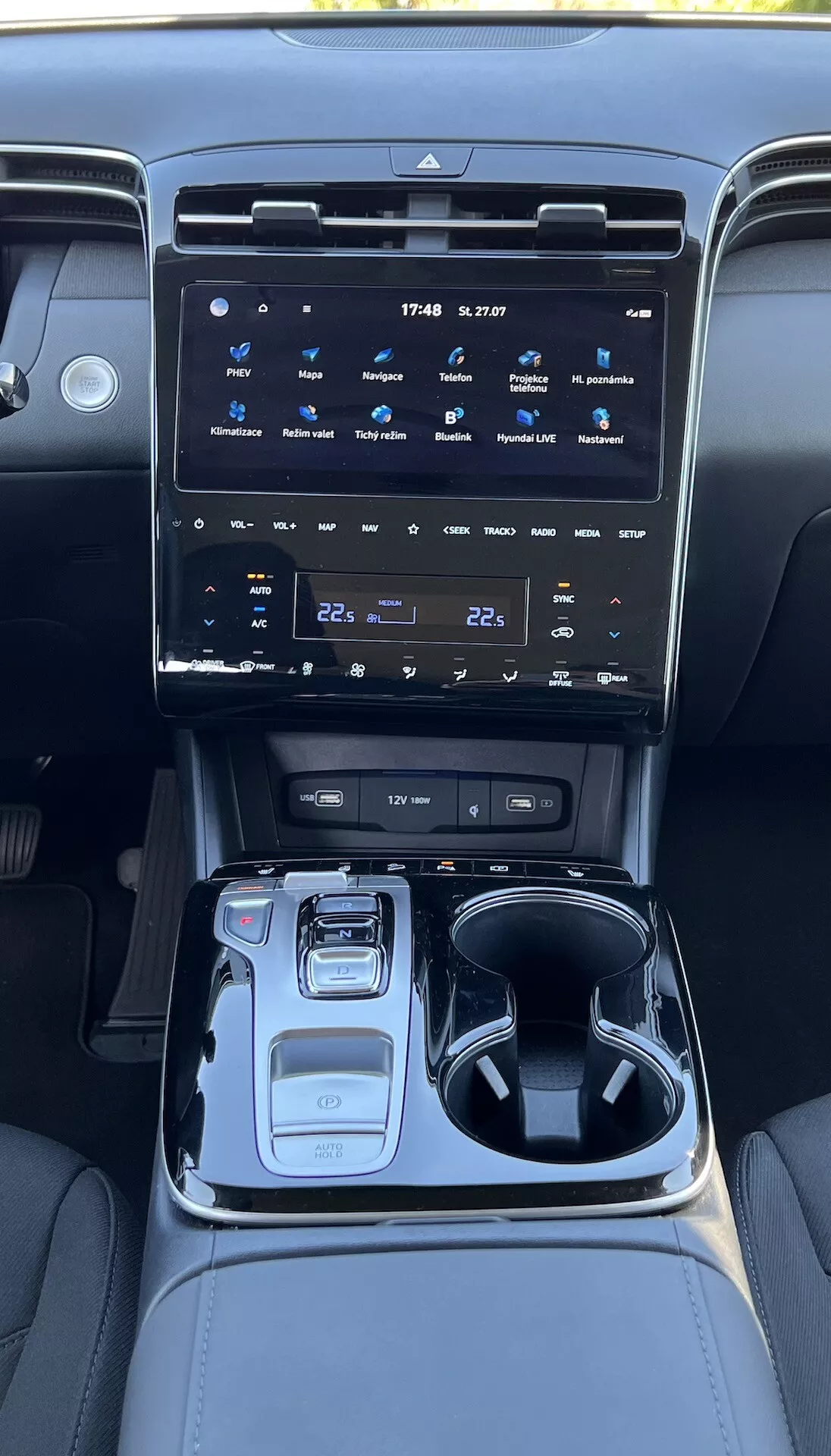 Notranjost Hyundai Tucson 2020 prikazuje sredinsko konzolo z velikim zaslonom na dotik za informacijsko-razvedrilni sistem, gumbi za klimatsko napravo, elektronskim izbirnikom prestav, izbirnikom načina vožnje, držali za skodelice, predalom za shranjevanje in ambientalno osvetlitvijo.