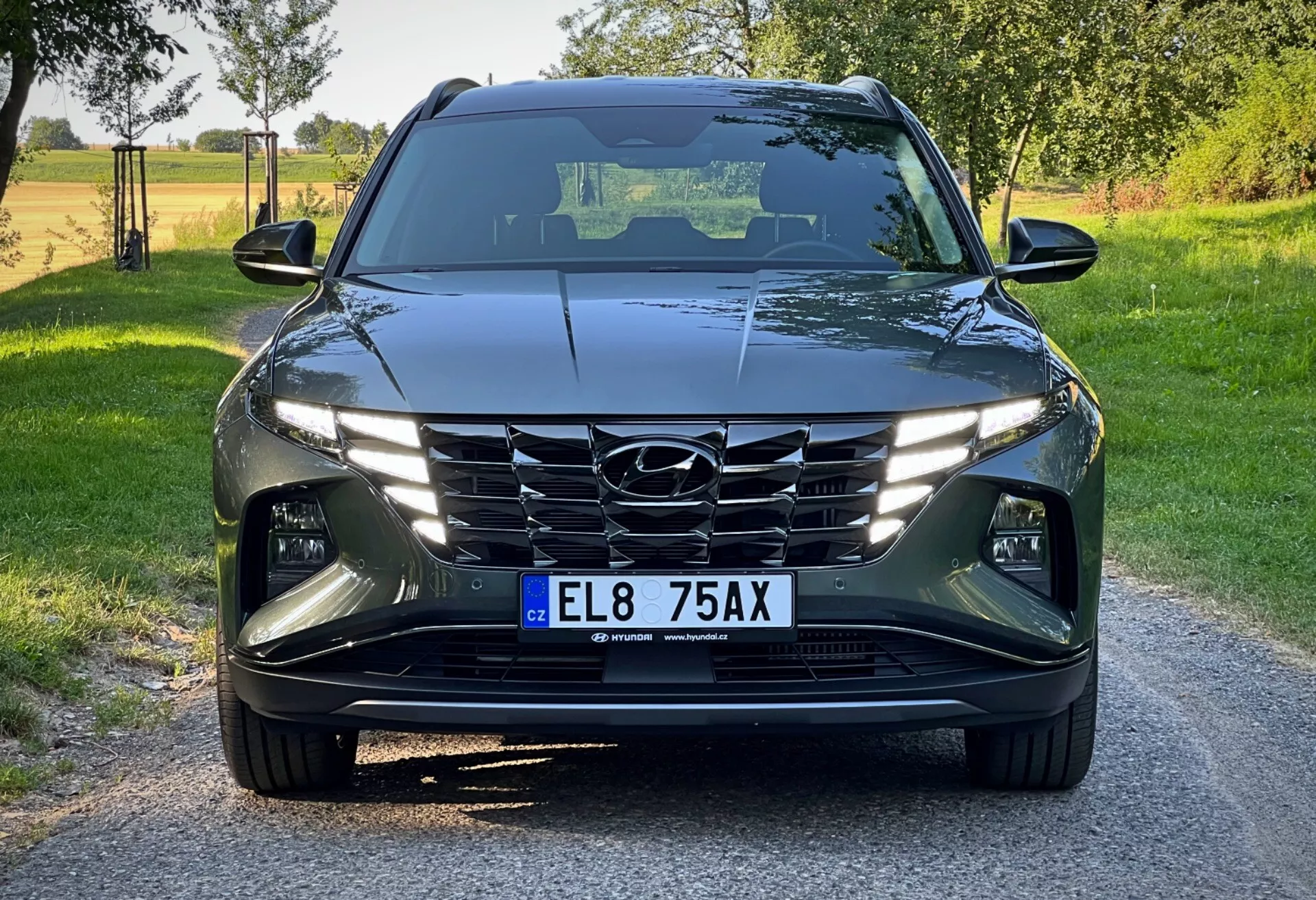 Hyundai Tucson 2020, prikazan z nizkega sprednjega kota, ki prikazuje njegov sodoben dizajn z ostrimi, kotnimi linijami, LED žarometi, kaskadno masko in naprednimi voznimi pomočnimi sistemi na svetlem podeželskem ozadju