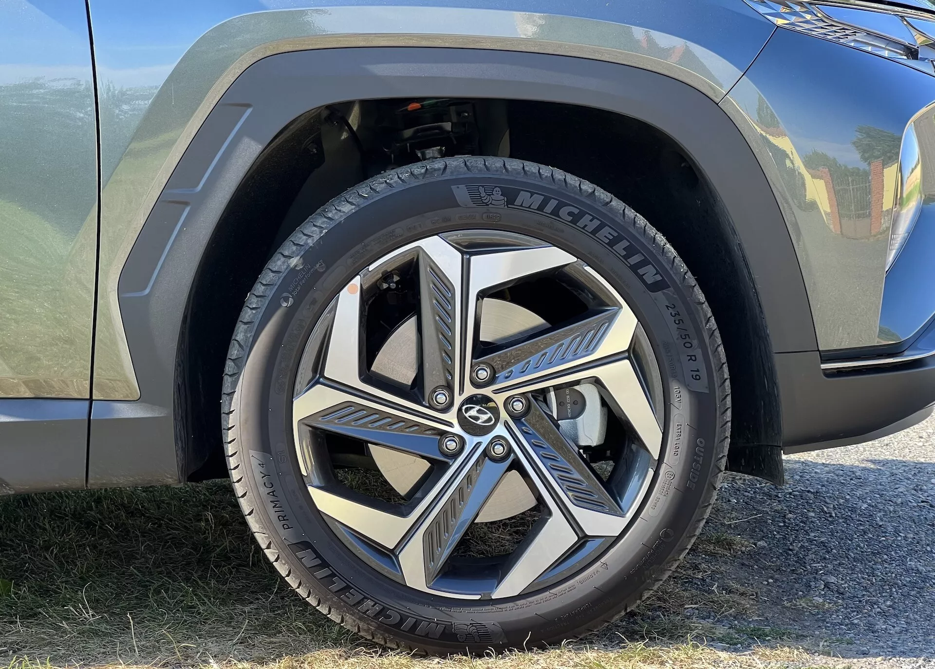 Podroben pogled na sprednje kolo in del blatnika Hyundai Tucsona 2020, z Michelinovo pnevmatiko in dinamičnim večkrakim dizajnom zlitinskega platišča, kar poudarja sodobno avtomobilistično estetiko in blagovno znamko