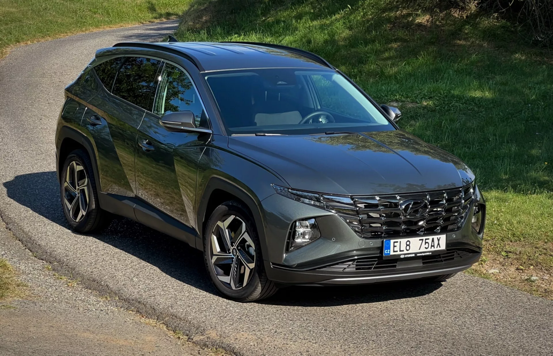 SUV Hyundai Tucson 2020 parkiran na osamljeni cesti, ki prikazuje svojo sprednjo rešetko, LED žaromete, zlitinska kolesa in linije karoserije pod naravno sončno svetlobo