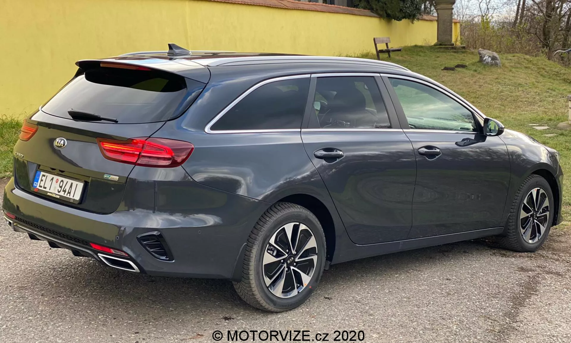 Temnosiv kovinski Kia Ceed 2018, prikazan iz tričetrt zadnjega pogleda, poudarjajoč njegov sodoben dizajn hatchbacka ali karavana z nagnjenim zadnjim oknom, integriranim zadnjim spojlerjem, večkrakimi aluminijastimi platišči, kljukami vrat in stranskimi ogledali v barvi karoserije verjetno z vgrajenimi smerniki, značilni horizontalni zadnji svetlobni sklop verjetno z LED tehnologijo, anteno plavuti morskega psa, dvojnimi izpušnimi cevmi, visoko nameščeno tretjo zavorno lučjo, možnost odmrzovanja zadnjega okna, senzorji ali odsevniki, ki nakazujejo sistem pomoči pri parkiranju zadaj, fotografirano od blizu z nevtralno osvetlitvijo.