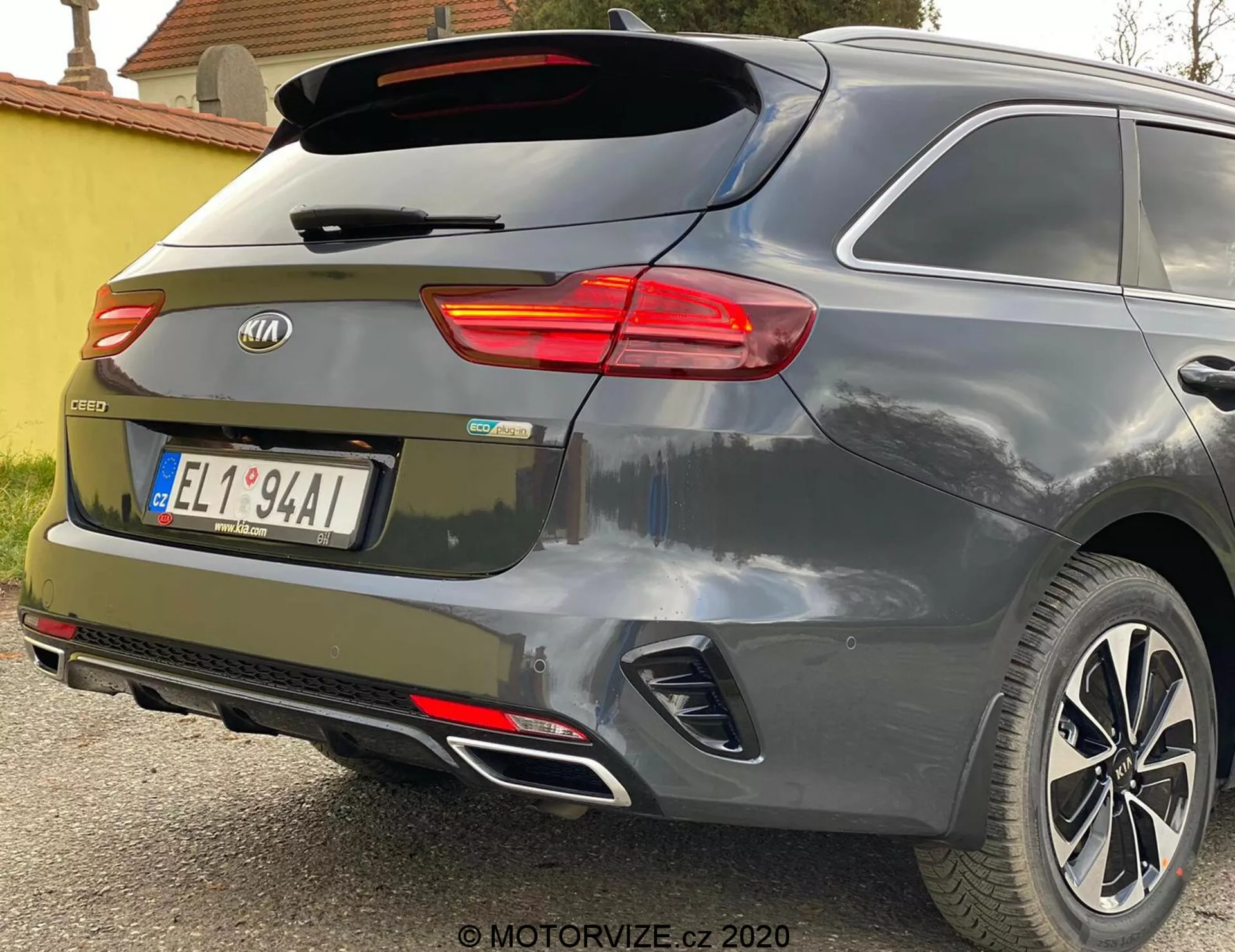 Delni zadnji kotni pogled na Kia Ceed 2018, ki poudarja osvetljeno desno zadnjo luč, zadnje steklo z brisalcem, zadnja vrata z značko znamke in oznako modela 'CEED', vgrajene odsevnike v zadnjem odbijaču, parkirne senzorje, dvojni izpušni sistem in lita platišča v kovinsko sivi ali srebrni barvi.