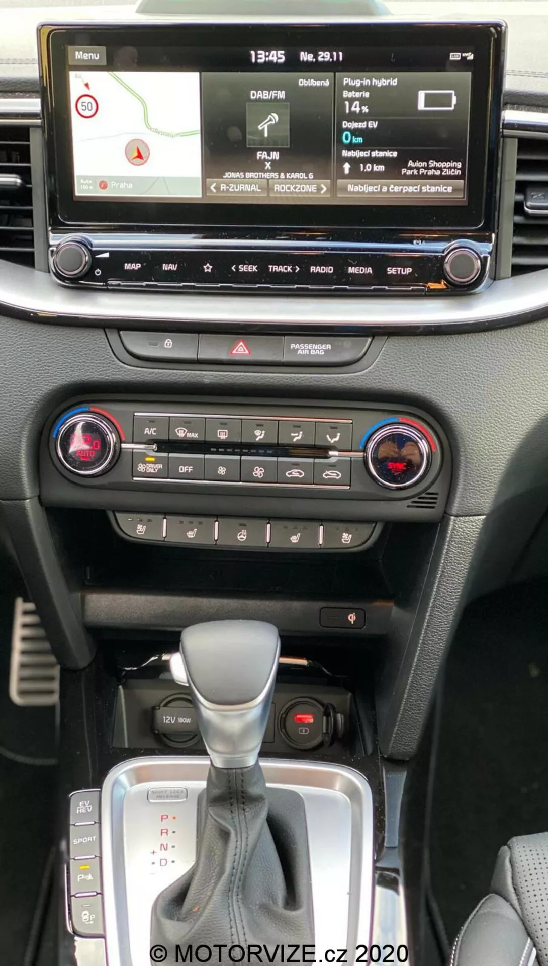 Notranjost Kia Ceed 2018, prikazuje osrednjo konzolo z vidika potnika v prvi vrsti, z digitalnim zaslonom za infozabavni sistem, navigacijski zemljevid, predvajalnik medijev, nastavitve vozila, klimatske kontrole z dvozonskim sistemom, gumb za opozorilne luči, samodejni menjalnik z usnjenim mehom in režo za ključ brez ključa.