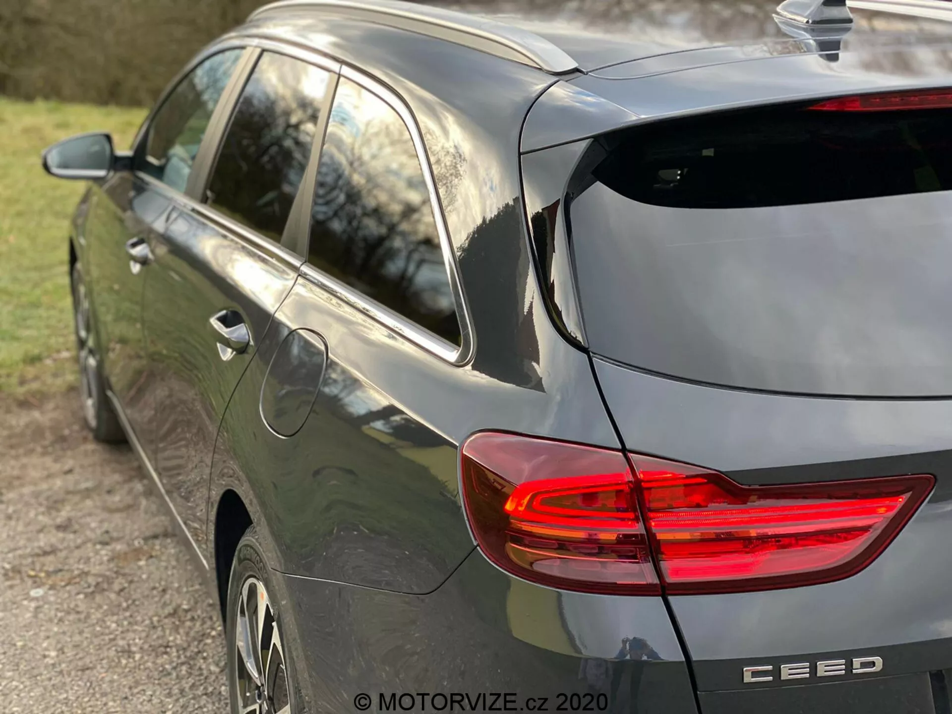 Delni stranski in zadnji pogled na moderen sive barve hatchback Kia Ceed 2018, ki poudarja osvetljeno zadnjo luč LED v obliki črke C, dizajn hatchbacka z zadnjim brisalcem in subtilnim strešnim spojlerjem, anteno v obliki plavuti morskega psa, litkaste platišča in značko blagovne znamke z imenom modela 'CEED', posneto v naravni svetlobi poznega popoldneva in z majhno globino polja, osredotočeno na vozilo.