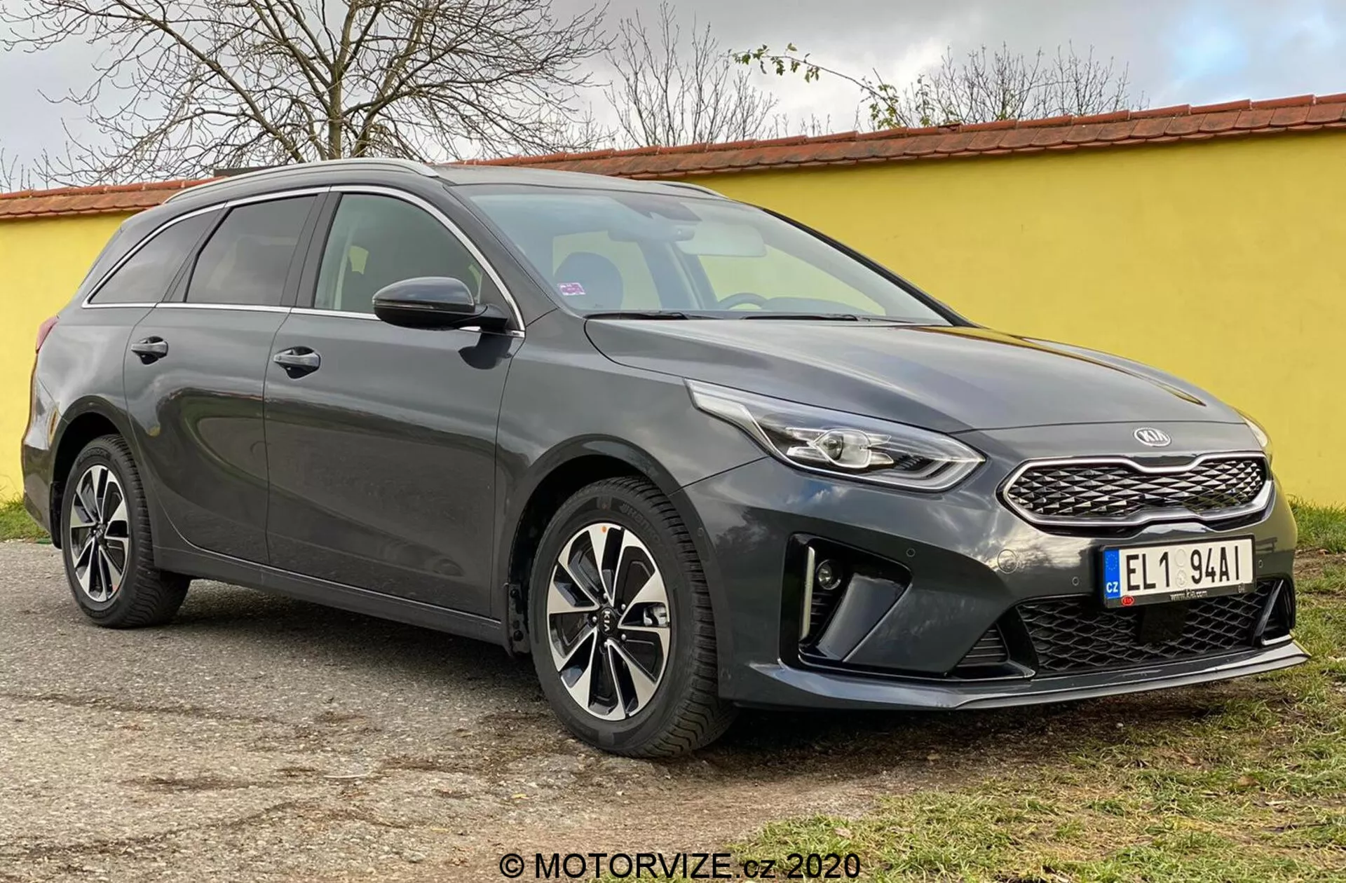 Slika prikazuje Kia Ceed 2018, sodobno karavan vozilo, ujeto z kotom spredaj treh četrtin, poudarjajoč njegovo sprednjo fasado, vključno s strukturirano masko s prepoznavnim emblemom blagovne znamke, ozke žaromete, ki se vračajo nazaj z LED dnevnimi lučmi in sprednji odbijač z ohišji za meglenke in parkirnimi senzorji. Elegantne linije pokrova motorja vodijo do ostro nagnjenega vetrobranskega stekla, kar poudarja aerodinamični profil avtomobila. Vidna so večkraka aluminijasta platišča in stranska ogledala z integriranimi smerniki, skupaj z nagnjeno strešno linijo proti zadnjemu delu in strešni nosilci, kar poudarja tako slog kot uporabnost. Zatemnjena okna in linije karoserije vzdolž strani še poudarijo izklesan videz. Avto miruje na ravni zunanji površini.