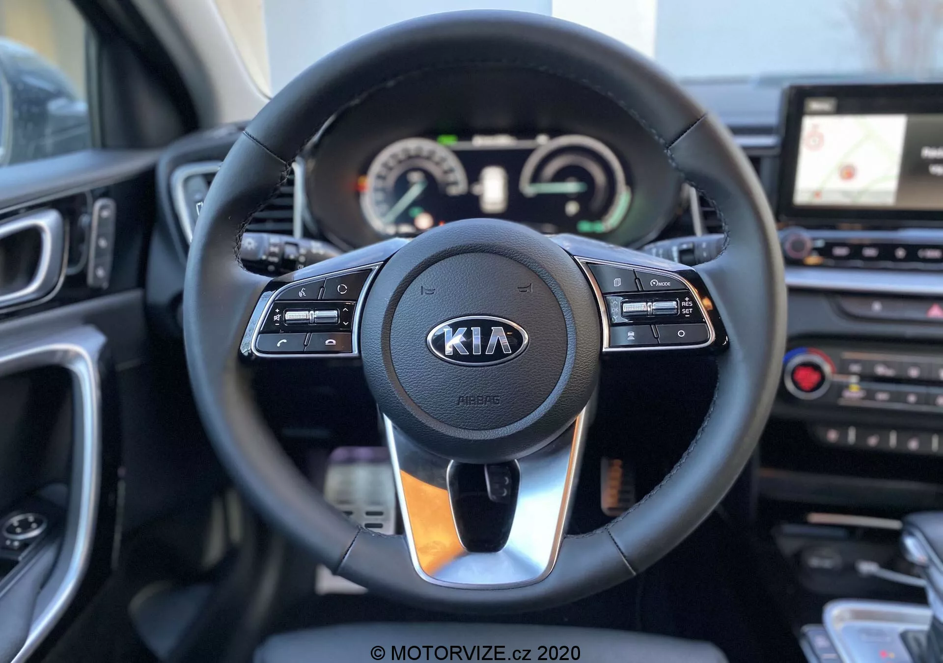 Notranjost Kia Ceed 2018 s poudarkom na volanu in armaturni plošči s perspektive voznika. Moder volan ima nameščene komande za tempomat, interakcijo z multimedijami in prostoročno komunikacijo, z izstopajočim logotipom Kia. Za volanom je instrumentna plošča, ki združuje analogne merilnike in digitalni zaslon, ki prikazuje hitrostnik in obratomer, poleg večfunkcijskega zaslona. Desno od volana je vidna del osrednje konzole z zaslonom na dotik infotainment sistema in navigacijo GPS, ter tipke za nadzor klimatske naprave. Slikovna kvaliteta je jasna z plitko globino polja, kar poudari volan in njegovo neposredno okolico.