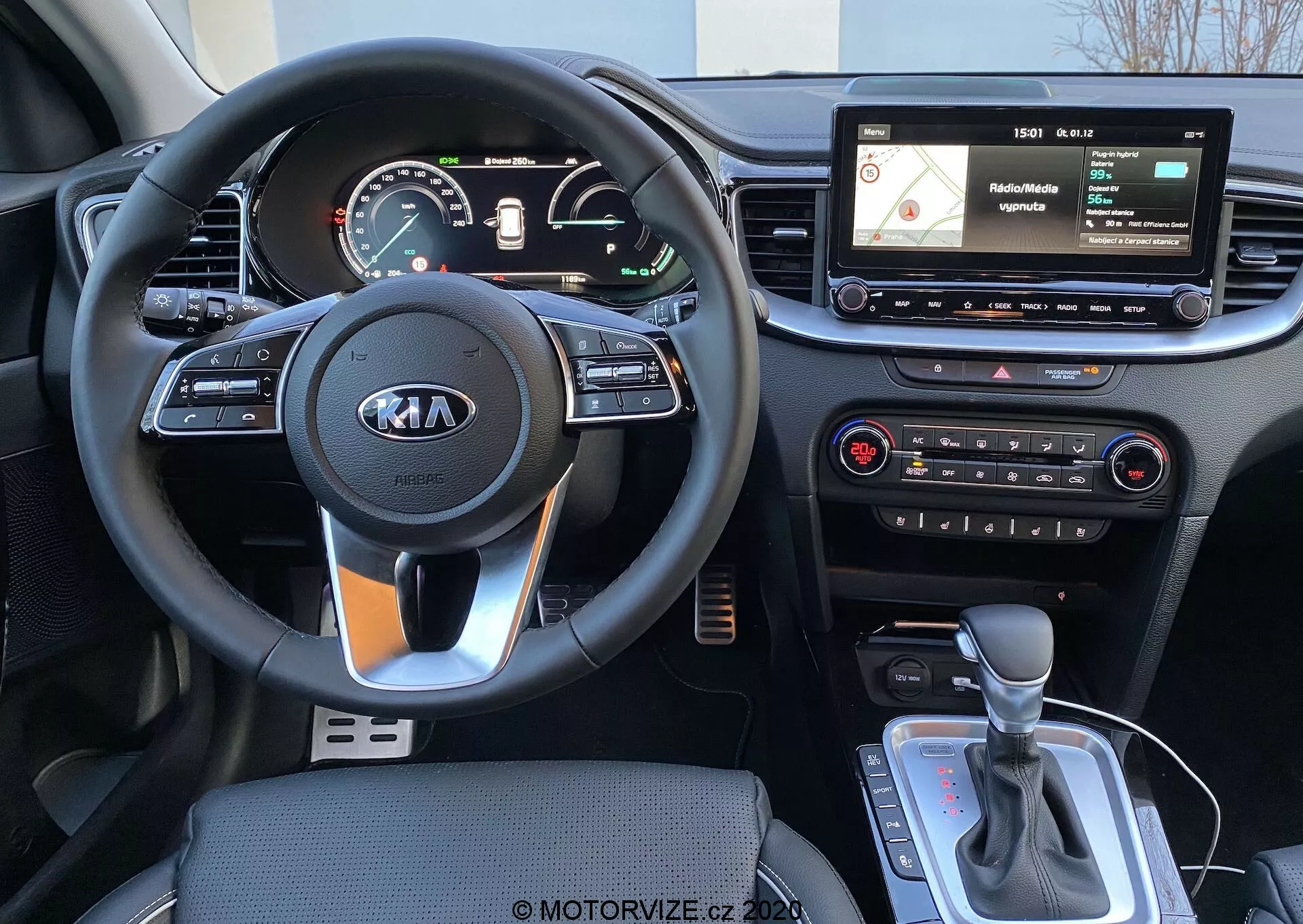 Notranji pogled Kie Ceed 2018 iz perspektive voznika, ki prikazuje trikraki volan z logotipom Kia, krmilne gumbe na volanu, kombinirano analogno in digitalno instrumentno ploščo, lebdeči zaslon infozabavnega sistema z navigacijo in medijskim vmesnikom, fizične kontrole klimatske naprave ter ročico samodejnega menjalnika z morebitnim izbirnikom načina vožnje ali elektronsko parkirno zavoro.