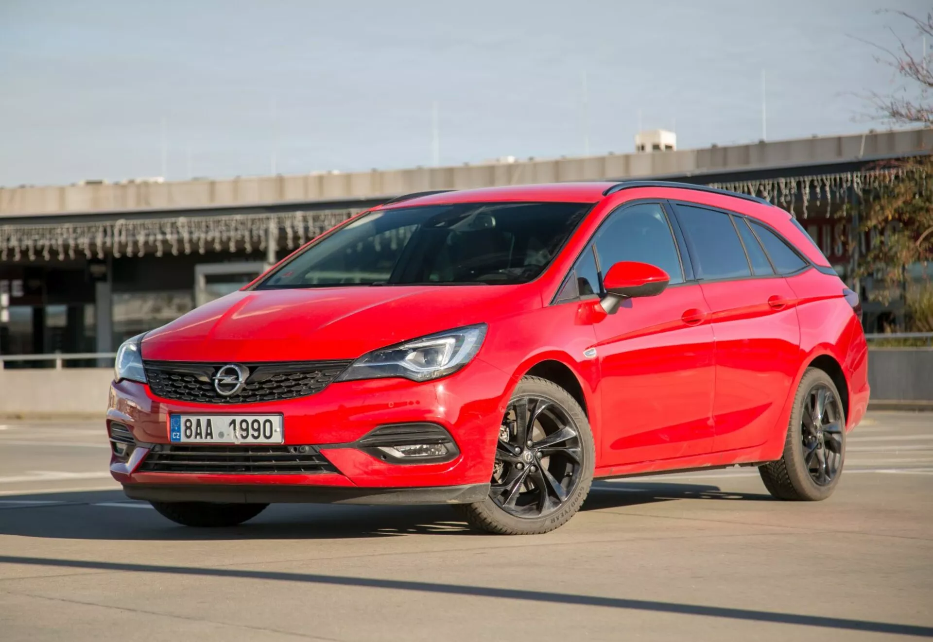 Svetlo rdeč hatchback Kia Ceed letnik 2009 parkiran na gladkem betonu pod jasnim nebom, prikazuje LED žaromete, elegantno rešetko, temna lita platišča in sodobno aerodinamično zasnovo iz kota tri četrtine spredaj čez dan.