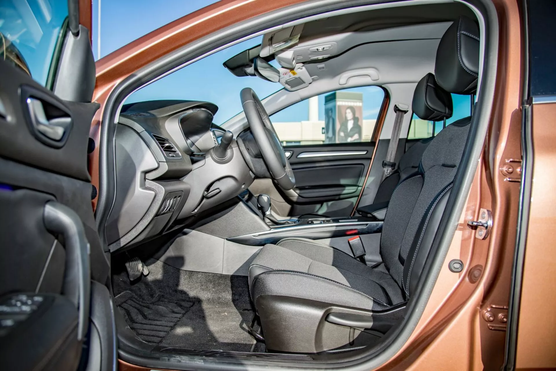 Notranji pogled Kia Ceed Pro-Cee'd 2009 skozi odprta voznikova vrata, ki prikazuje sprednje sedeže iz temnega blaga, integrirane kontrole na volanu, delno vidno armaturno ploščo z zaslonom za infotainment, sredinsko konzolo z ročico za prestavljanje, talne preproge in dvobarvno barvno shemo