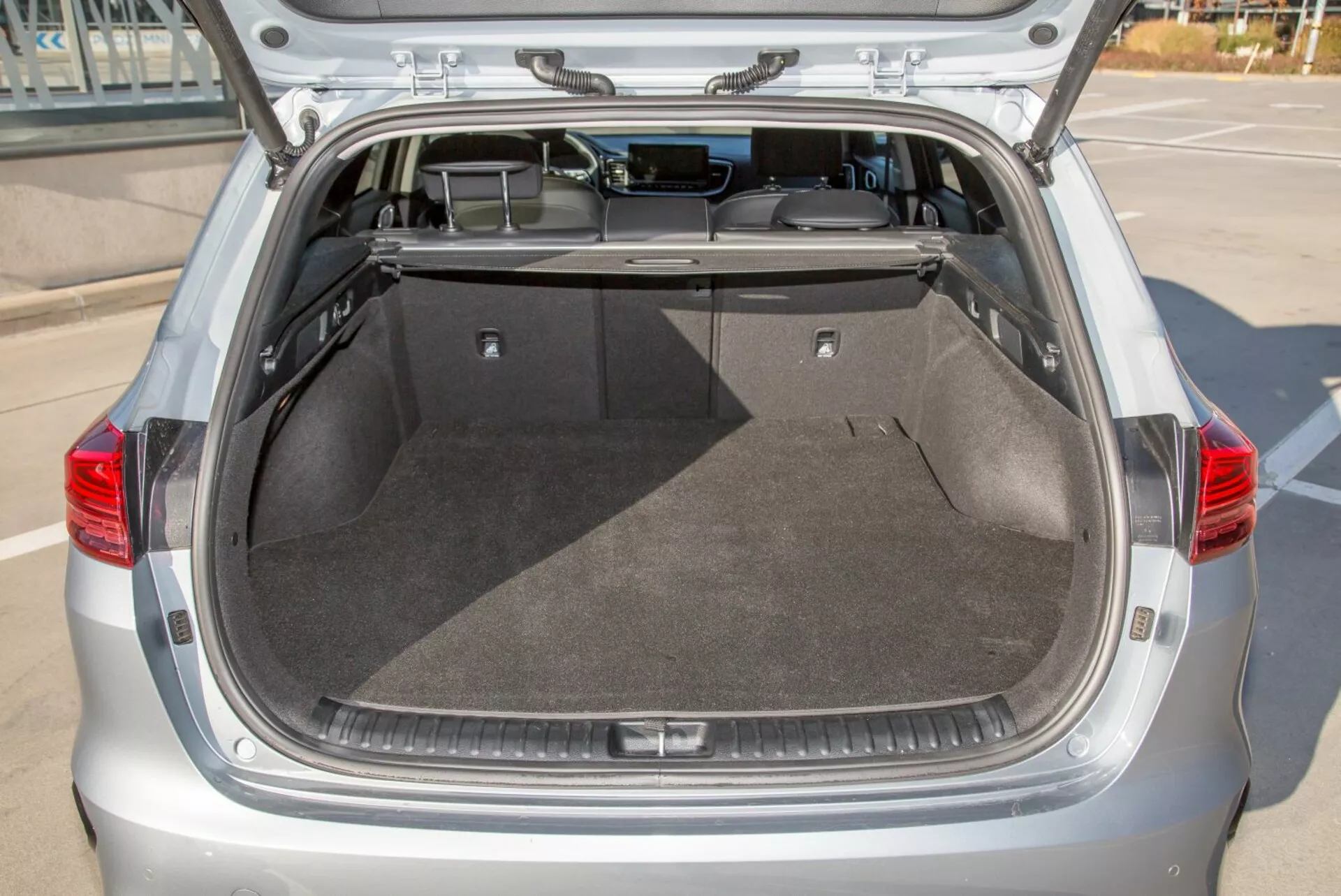 Zadnji prtljažni prostor hatchbacka Kia Cee'd 2009 z odprtim pokrovom, ki prikazuje prostorno čisto tovorni prostor, preprogo, zložljivo prevleko in potencialno notranjo razsvetljavo