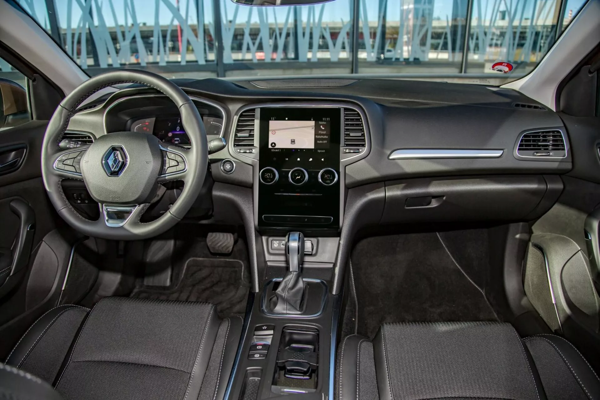 Notranjost Kia Cee'd 2009 iz pogleda zadnjega sedeža, ki prikazuje večfunkcijski volan, zaslon na dotik informacijsko-razvedrilnega sistema, avtomatsko prestavno ročico in podrobnosti o oblazinjenju v predelu armaturne plošče