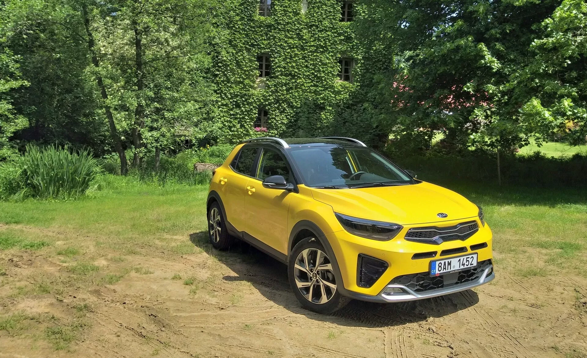 Živo rumeno crossover SUV Kia Stonic 2017 v tričetrtinskem sprednjem pogledu, ki poudarja njegovo sprednjo rešetko, LED žaromete, pokrov motorja in stran voznika, postavljeno proti naravnemu ozadju s sončno svetlobo na čistem terenu, razkazujejoče sposobnosti za lahko terensko vožnjo, športna platišča iz zlitine in moderne oblikovalske elemente.