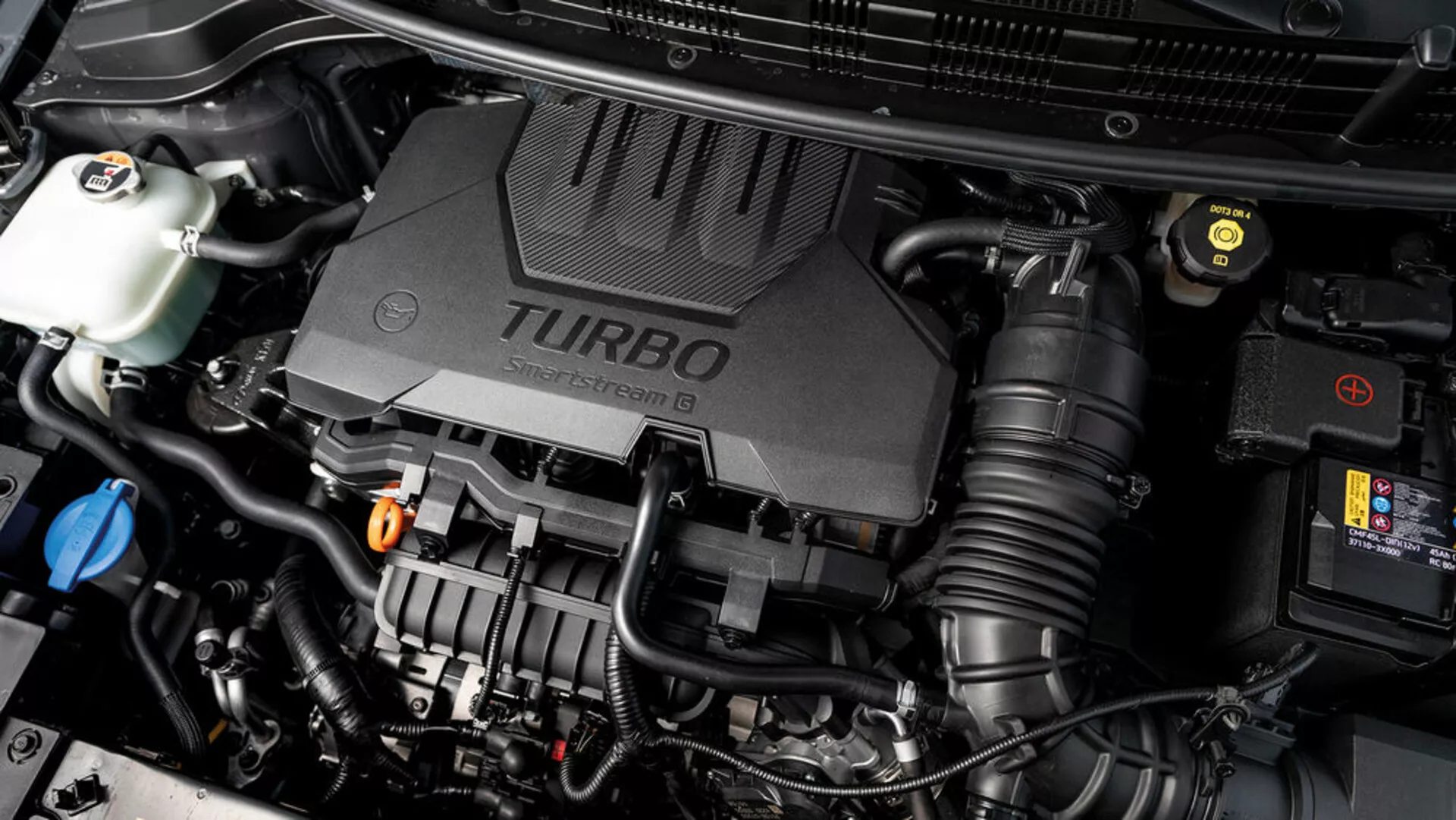Podroben pogled na motor Kia Stonic 2017 z pokrovom turbo motorja in različnimi vidnimi mehanskimi komponentami, ki prikazujejo tehnološke vidike vozila