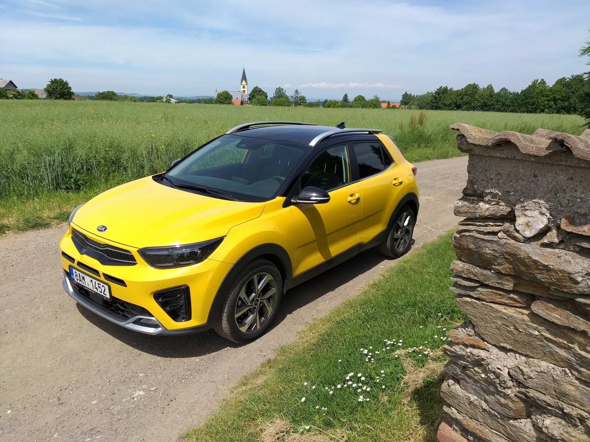 Svetlo rumen kompaktni SUV Kia Stonic 2017 s črno streho, ki prikazuje svoj eleganten dizajn in dinamične obrise iz kota treh četrtin na podeželski makadamski poti