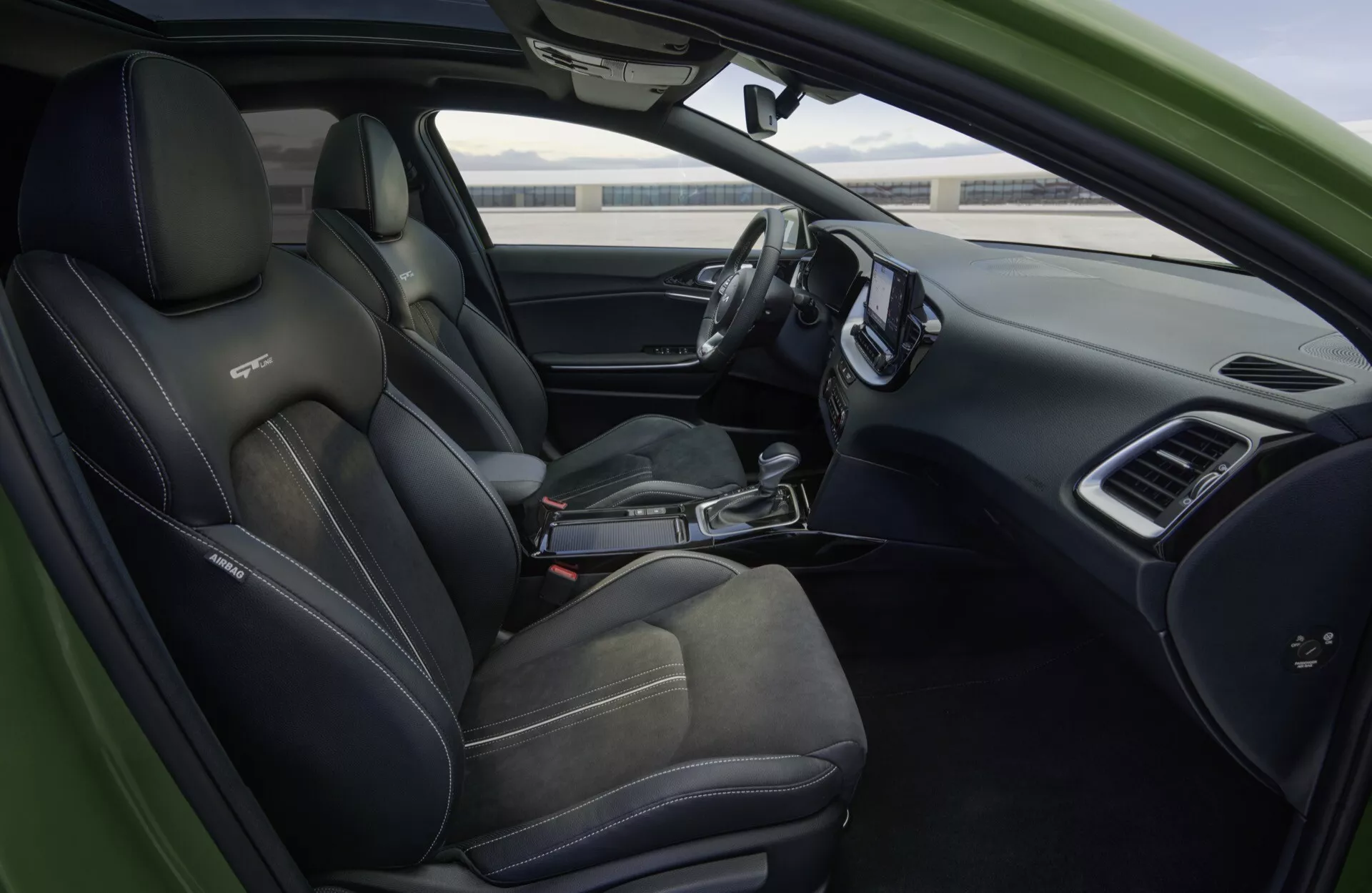 Notranji pogled na Kia XCeed 2022 CD-facelift s športnimi črnimi sedeži z nasprotujočimi šivi, usnjenim volanom z ravnim dnom z multifunkcijskimi gumbi, elegantno armaturno ploščo z velikim zaslonom za infotainment, digitalnim merilnikom, avtomatskim izbirnikom prestav, in nadzorom na voznikovih vratih, kar vsebuje sodobno avtomobilsko tehnologijo in luksuzne lastnosti.