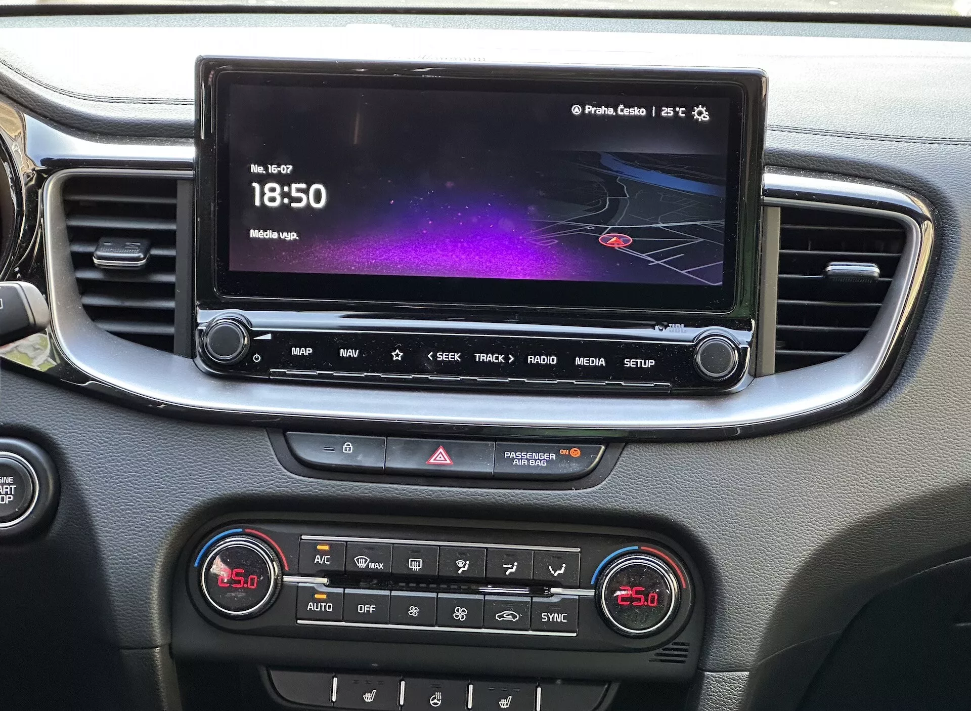 Podroben pogled na notranjost Kia Xceed 2022, ki prikazuje sredinsko konzolo z zaslonom na dotik za infotainment, ki prikazuje barvni vmesnik z navigacijo in medijskimi informacijami, vrsto hitrih dostopnih gumbov, kontrolnik za opozorilne luči in ploščo z dvojno območno klimatsko napravo, vse obrobljeno s srebrnim okrasjem.