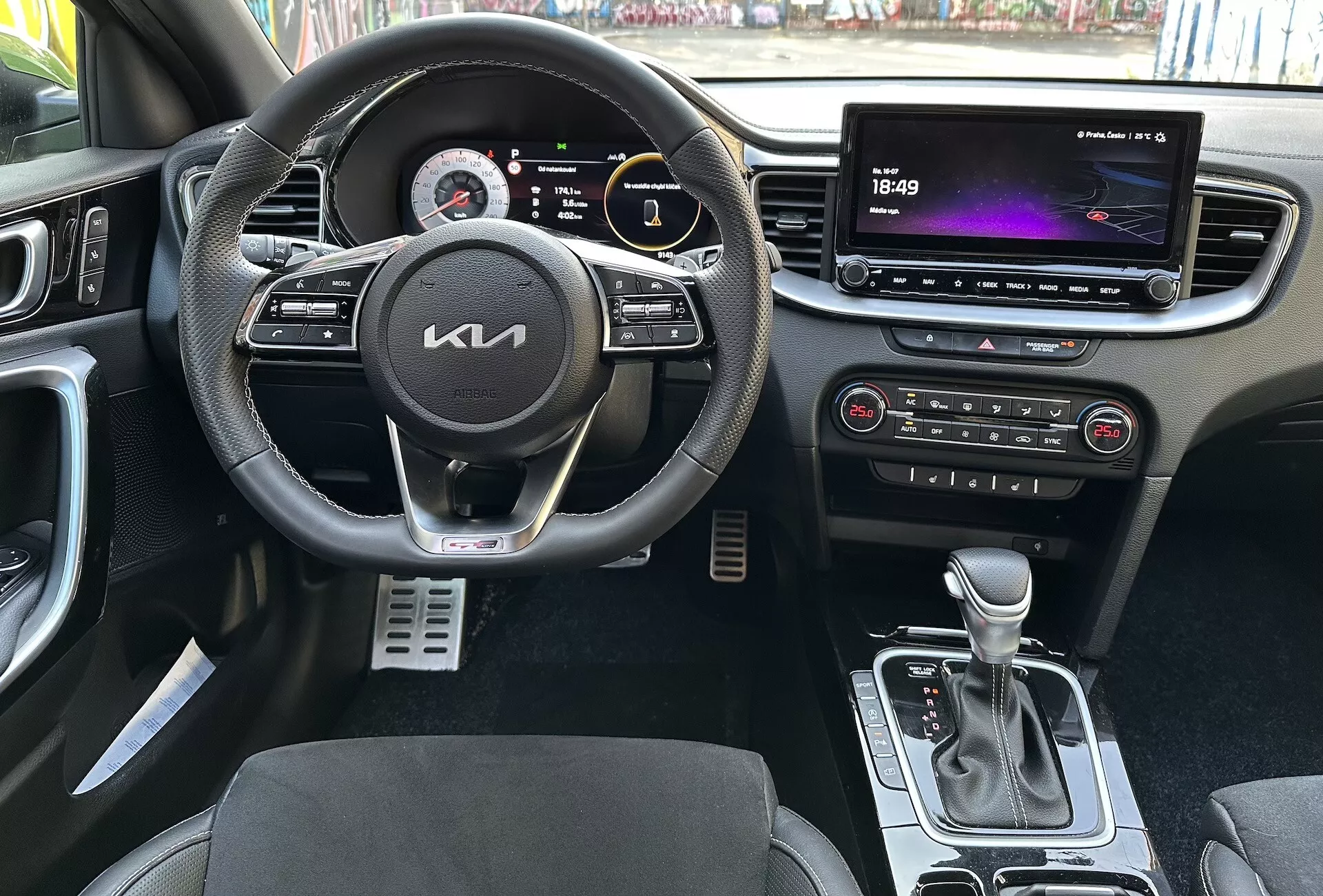 Notranji pogled Kia XCeed 2022, ki poudarja vozniku namenjene funkcije, kot so multifunkcijski usnjeni volan z gumbi za multimedio in tempomat, digitalna instrumentna plošča, velik zaslon na dotik infotainment sistema, avtomatska klimatska naprava, avtomatska prestavna ročica, sedeži z dvobarvnim oblazinjenjem in kovinskimi športnimi pedali iz perspektive prve osebe.