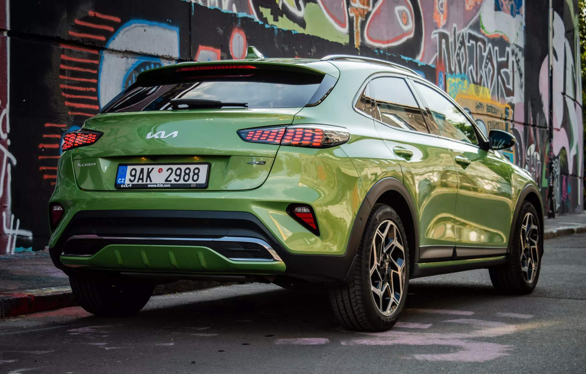 Sodoben križanec SUV Kia XCeed 2022 parkiran po diagonalu, ki prikazuje njegov desni zadnji del, z živahno zeleno barvo in temnimi zlitimi kolesi, prikazuje bočni profil vozila, zadnji dizajn, LED zadnje luči, zatemnjena okna, spojler na strehi in potencialni zadnji difuzor