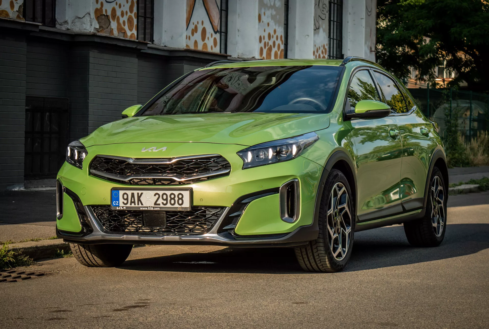 Kia XCeed 2022 v živahni apneni zeleni z LED žarometi, izstopajočo sprednjo masko z znamko znamke, športnim sprednjim odbijačem in velikimi zlitinskimi kolesi, osredotočena na tlakovano cesto z urbanim ozadjem