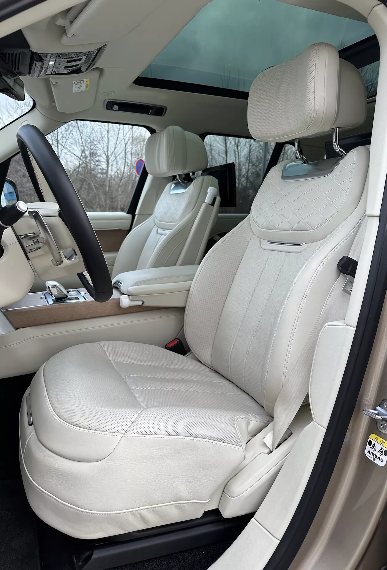 Pogled na notranjost Land Rover Range Rover 2021 z osredotočenjem na voznikovo stran z razkošnimi sedeži iz smetanovega usnja, multifunkcijskim volanom in naprednimi kontrolnimi elementi na sredinski konzoli