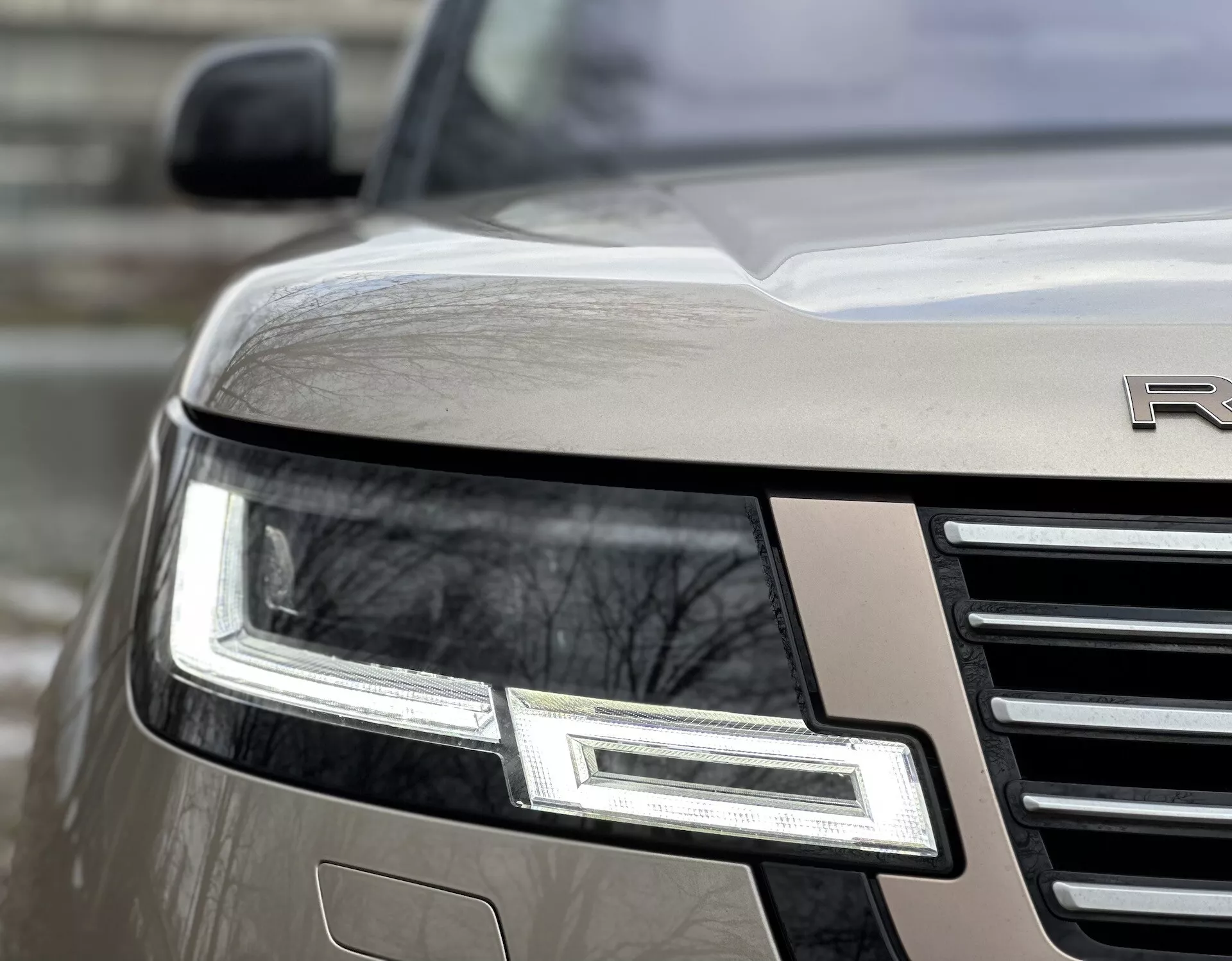 Podroben kotni pogled na sprednji kot Land Rover Range Rover iz leta 2021 z LED žarometom, kromirano rešetko in delnim emblemom na kovinskem telesu