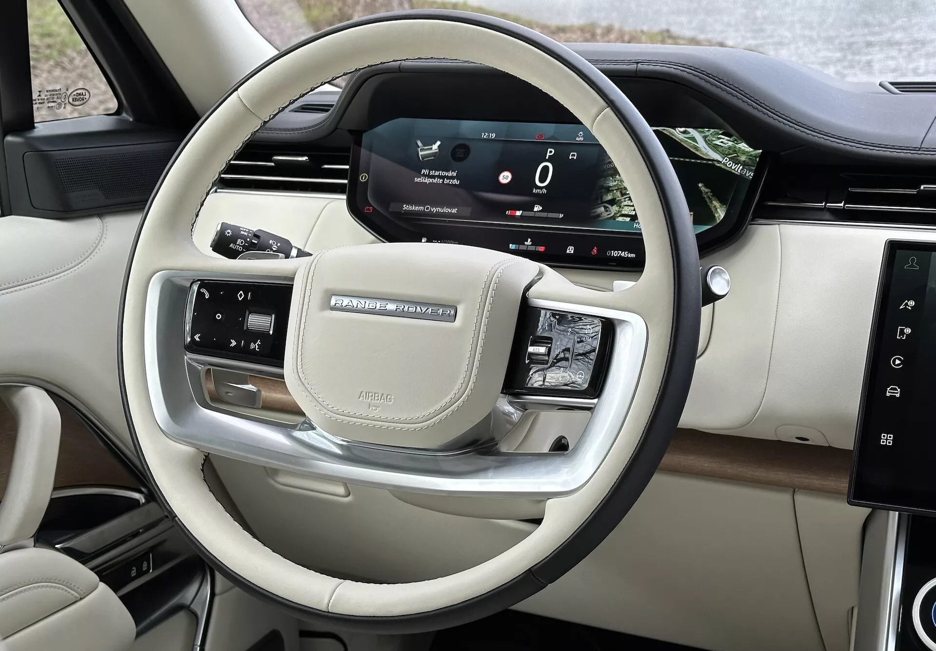 Pogled na notranjost Land Rover Range Rover 2021 s poudarkom na upravljalnih elementih na volanu in digitalni armaturni plošči voznika s kromiranimi dodatki in luksuznimi zaključki