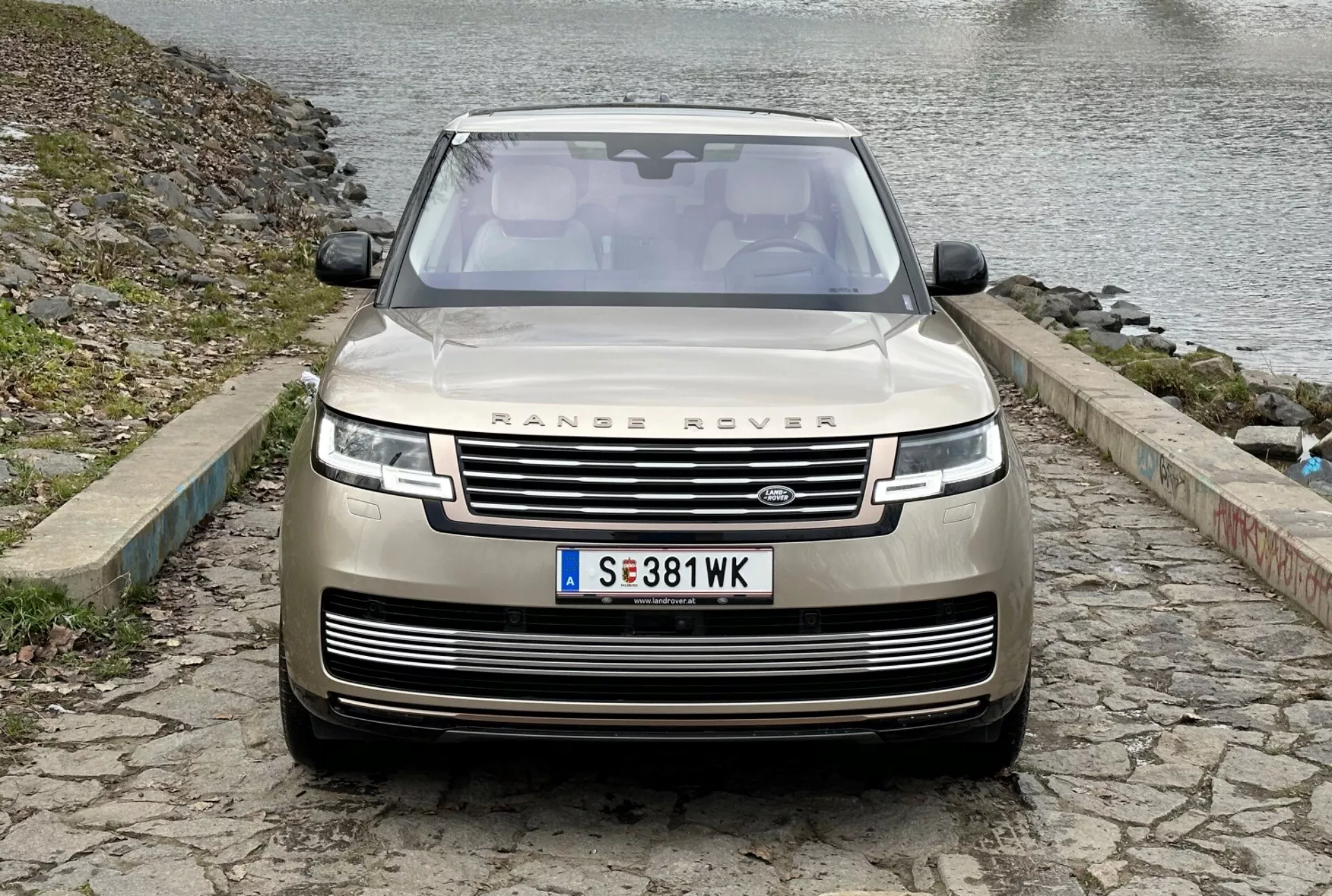 Range Rover 2021 v svetle metalik barvi, sprednji pogled, ki prikazuje mrežo, LED žaromete, senzorje za parkiranje in sprednjo kamero, parkiran na tlakovcih