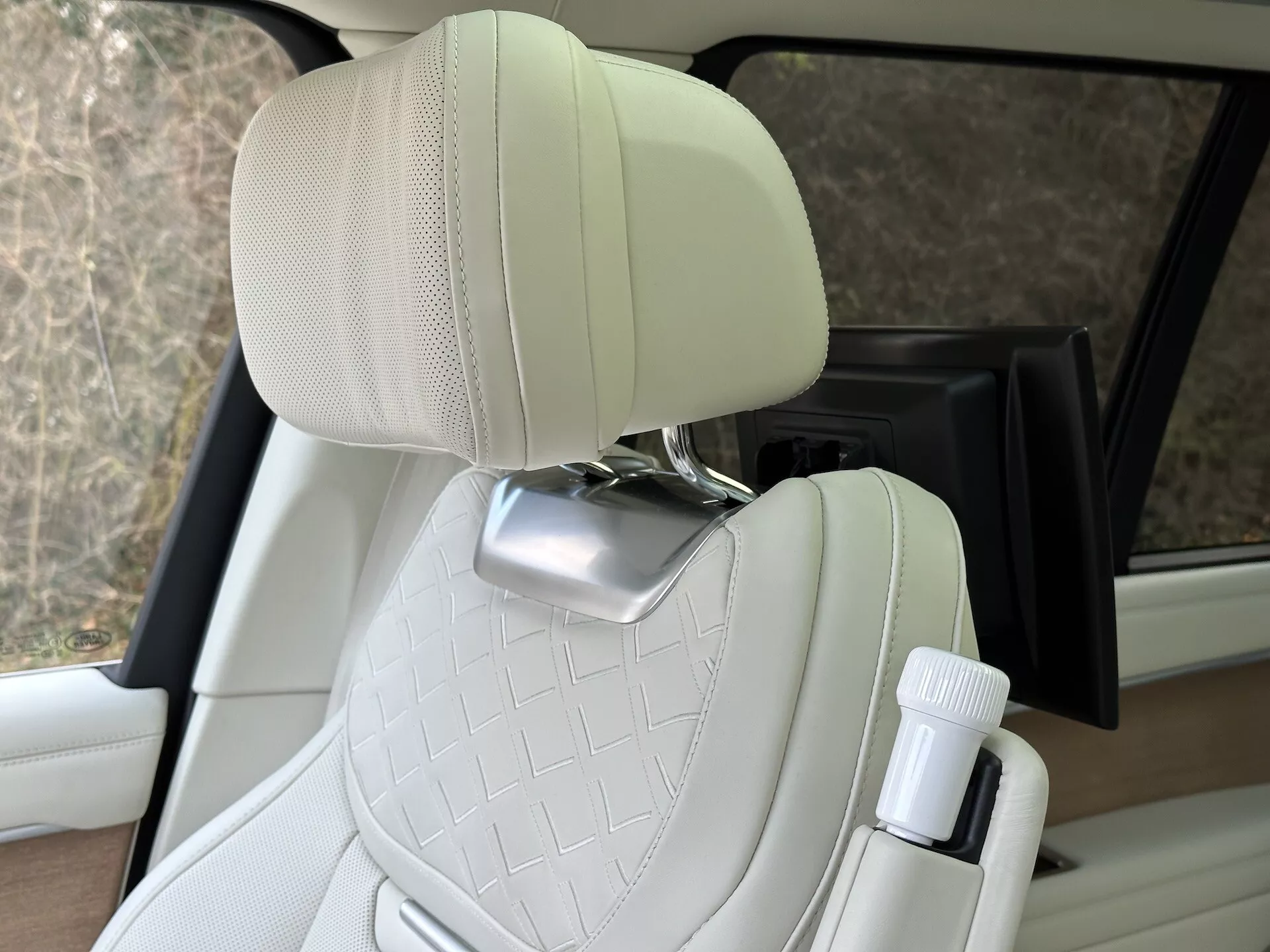 Notranjost Land Rover Range Rover 2021 z izpostavljenim prešitim potniškim sedežem iz smetanovega usnja s kromirano oporo za glavo in držalom za steklenico na strani vrat, ki prikazuje oblikovanje luksuznih vozil in lastnosti udobja