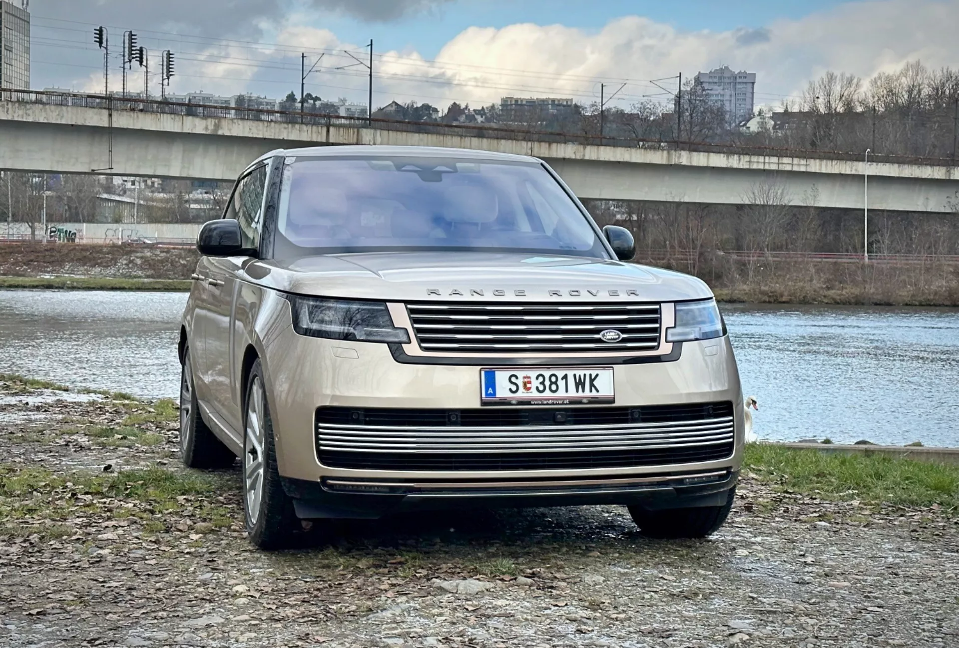 Luksuzni SUV Range Rover 2021, parkiran na prostem blizu reke in mostu v urbanih okoliščinah, predstavlja svoj moderni dizajn, sprednjo masko in elegantne LED žaromete