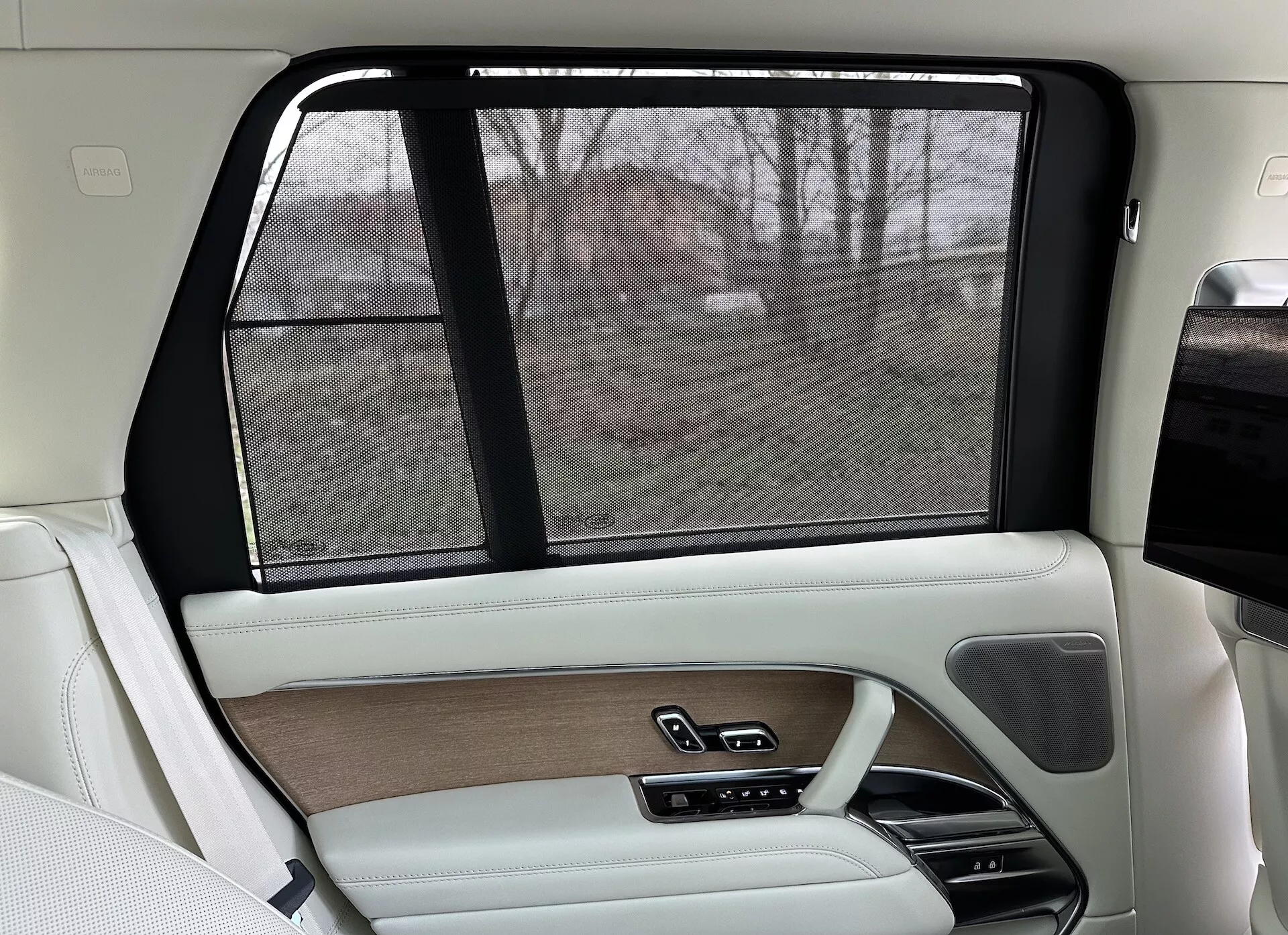 Notranjost desne zadnje strani Land Rover Range Rover 2021, z luksuzno obliko v bež in črni barvi, lesenimi obrobami, usnjenimi površinami, elektronsko sončno zaveso in naprednimi kontrolnimi sistemi