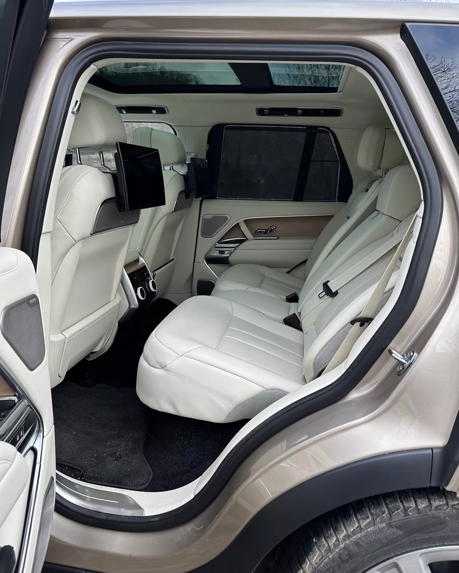 Notranji pogled na Land Rover Range Rover 2021, osredotočen na razkošni zadnji potniški prostor iz zunanje stranskega kota, z svetlo obarvanimi usnjenimi sedeži, napredno sredinsko konzolo, zabavnim sistemom in luksuznimi detajli