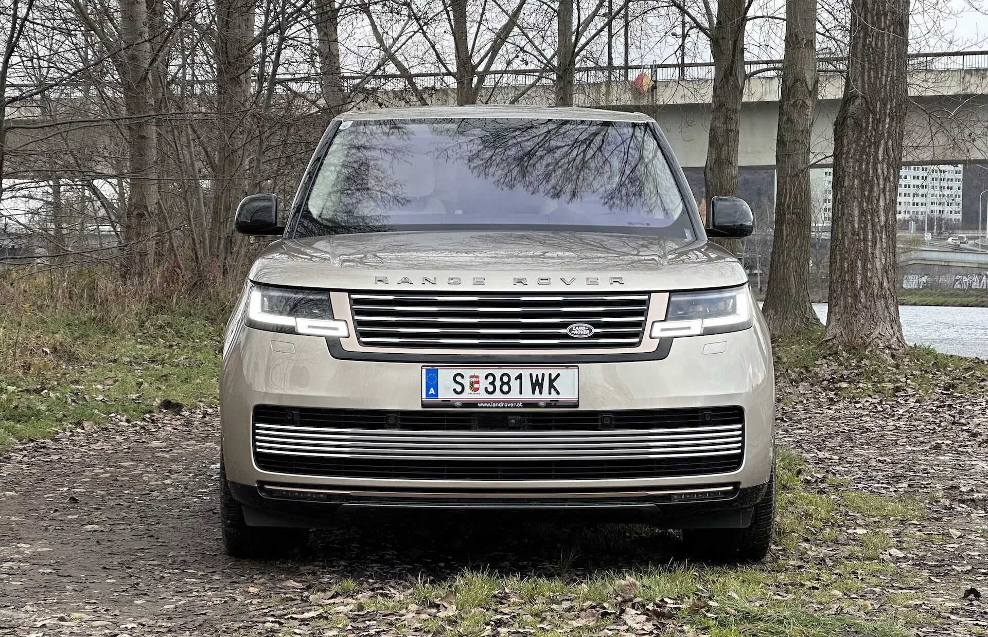 Sprednji pogled na Range Rover 2021, ki prikazuje rešetko, LED žaromete, napis 'RANGE ROVER' na pokrovu motorja in parkiran na neasfaltirani površini z delno podeželskim ozadjem