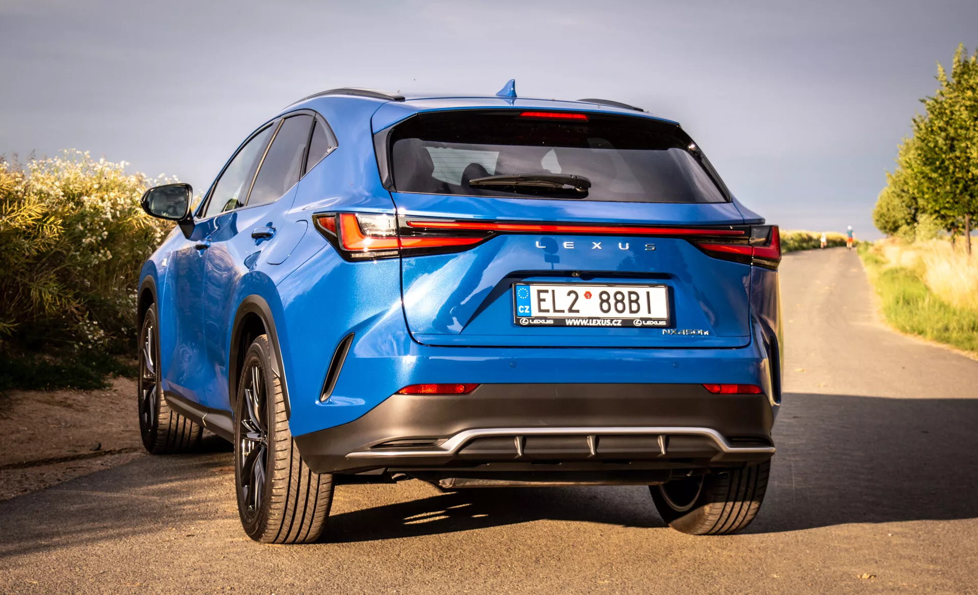 Zadnji pogled na luksuzni križanec SUV Lexus NX modre barve letnik 2021, ki prikazuje LED zadnje luči, znamko Lexus, športni zadnji odbijač z difuzorjem, dvojne izpušne cevi in druge tehnološke in oblikovalske značilnosti iz nizkega kota in perspektive treh četrtin