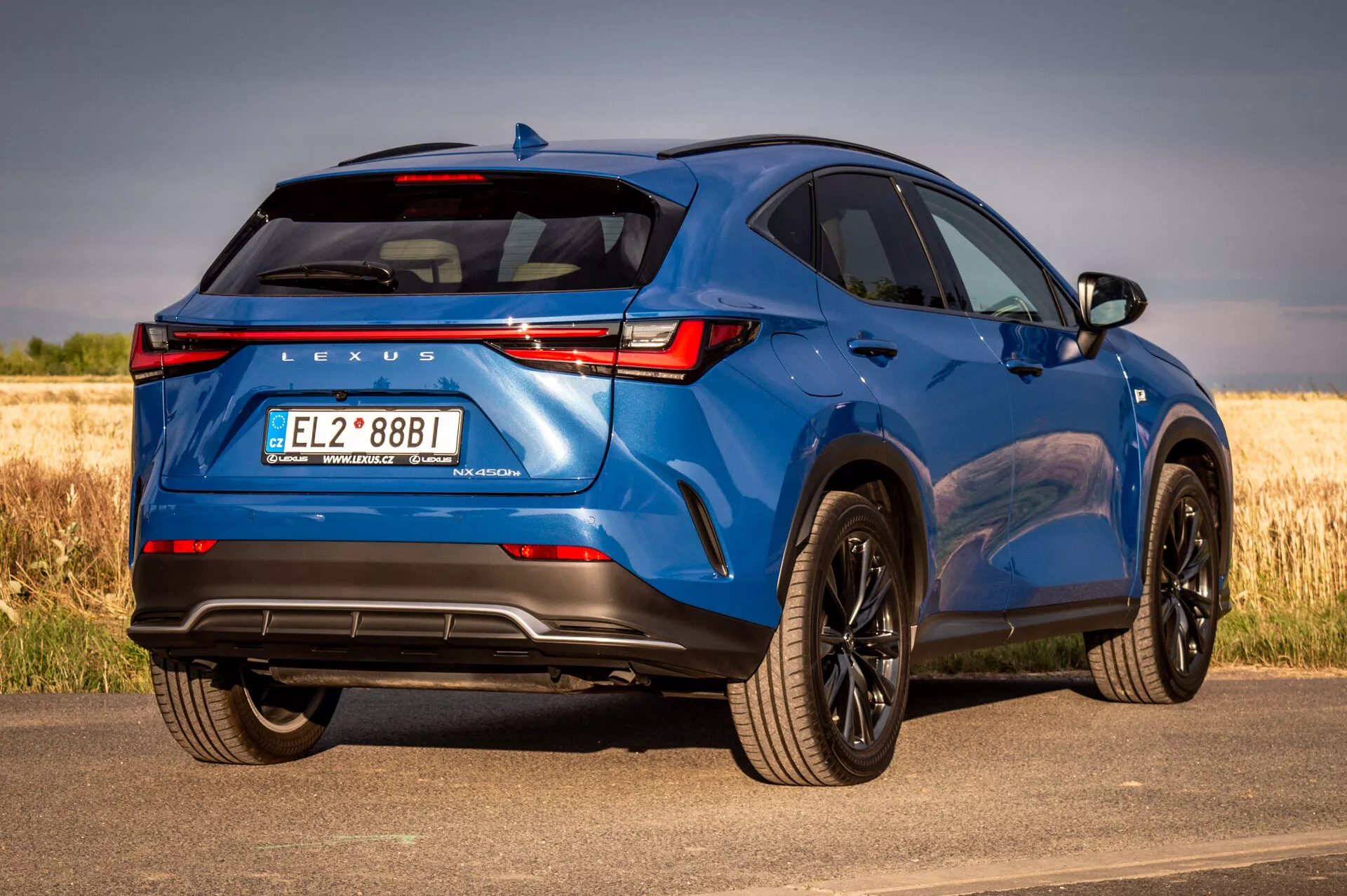 Modri SUV Lexus NX 2021 v pogledu s treh četrt zadajnje strani, ki prikazuje oblikovalske elemente in tehnološke lastnosti na sončen dan z naravnim ozadjem