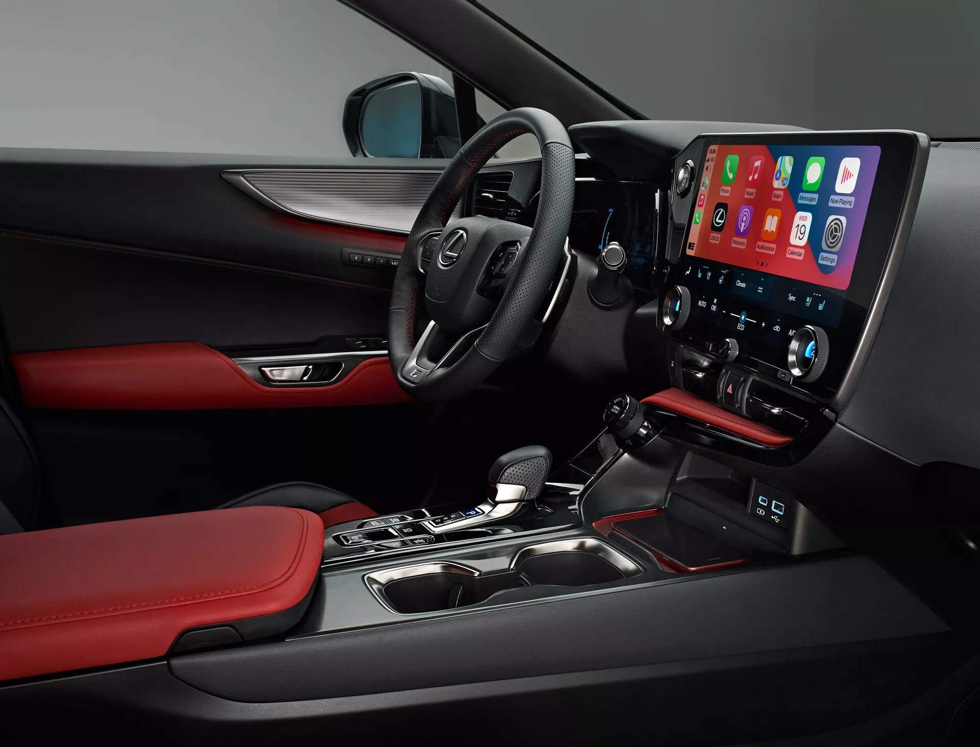 Pogled v notranjost Lexus NX 2021, ki prikazuje voznikovo stran. Slika zajema večfunkcijski volan z vgrajenimi kontrolami, delno vidno armaturno ploščo in izrazito sredinsko konzolo z velikim, navpično usmerjenim zaslonom za infotainment na dotik, ki verjetno prikazuje Apple CarPlay. Pod zaslonom so gumbi za dvopodročno nadzorovanje klime. Samodejna prestavna ročica, materiali in oblikovalske podrobnosti, kot so črne površine z rdečimi poudarki na sedežih in oblogah vrat ter delni pogled na kontrole na vratnem panelu voznika odražajo športni in prestižni značaj vozila.