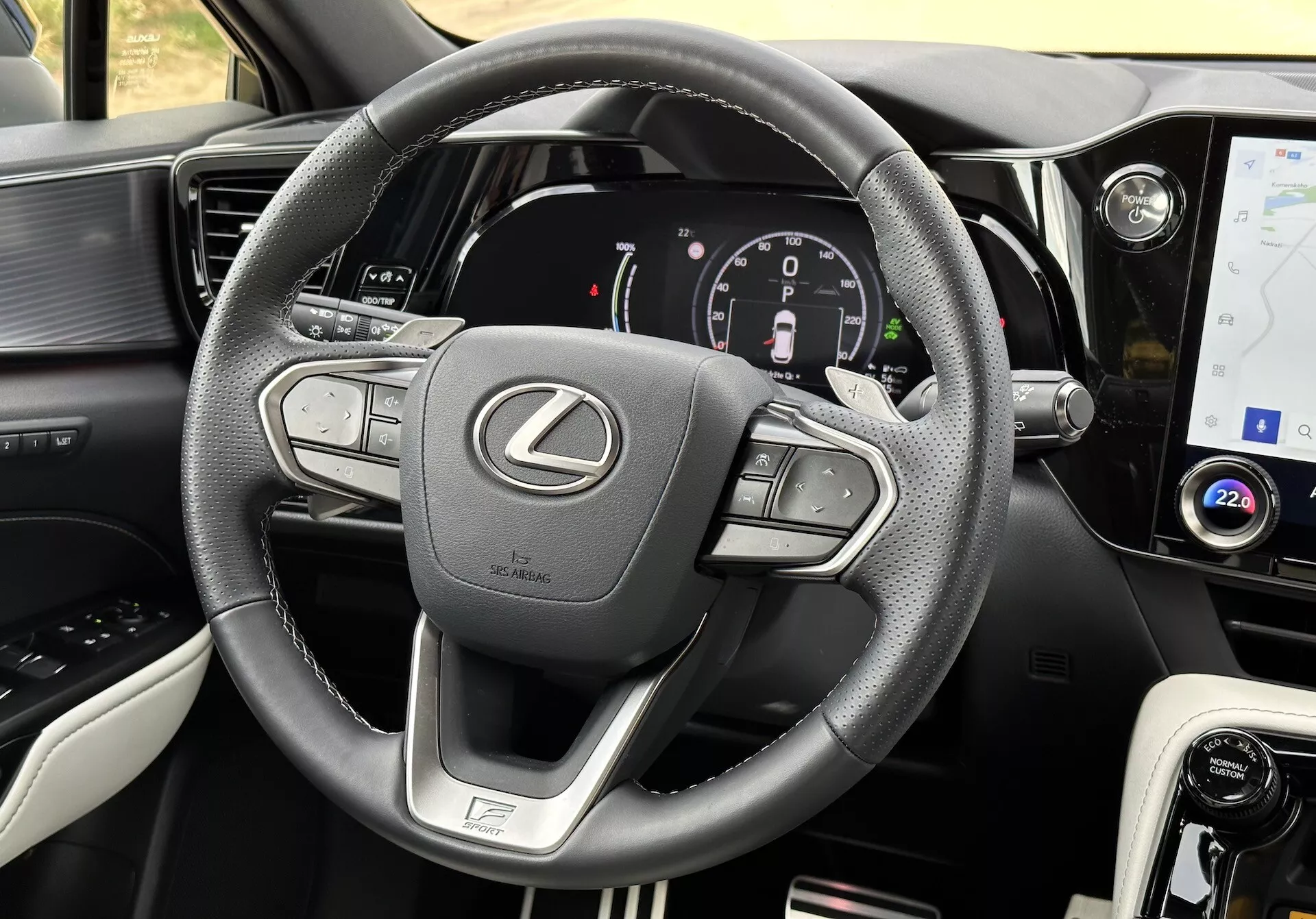 Pogled na notranjost Lexusa NX 2021 s poudarkom na volanu in armaturni plošči, ki prikazuje večfunkcijske gumbe, digitalno instrumentno ploščo, zaslon na dotik za informacije in zabavo, usnjene poudarke, izbirnik načina vožnje, zračnike in podrobne šive.