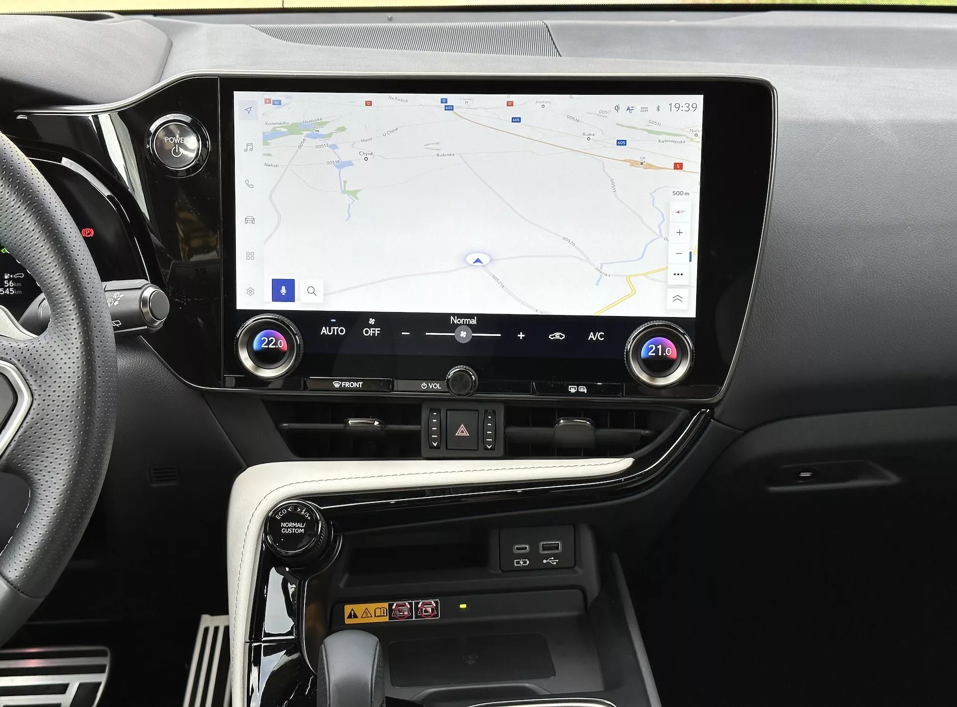 Sredinska konzola Lexus NX 2021 z zaslonom na dotik, ki prikazuje GPS navigacijo, gumbe in gumbke za upravljanje klime ter predel za brezžično polnjenje pametnega telefona