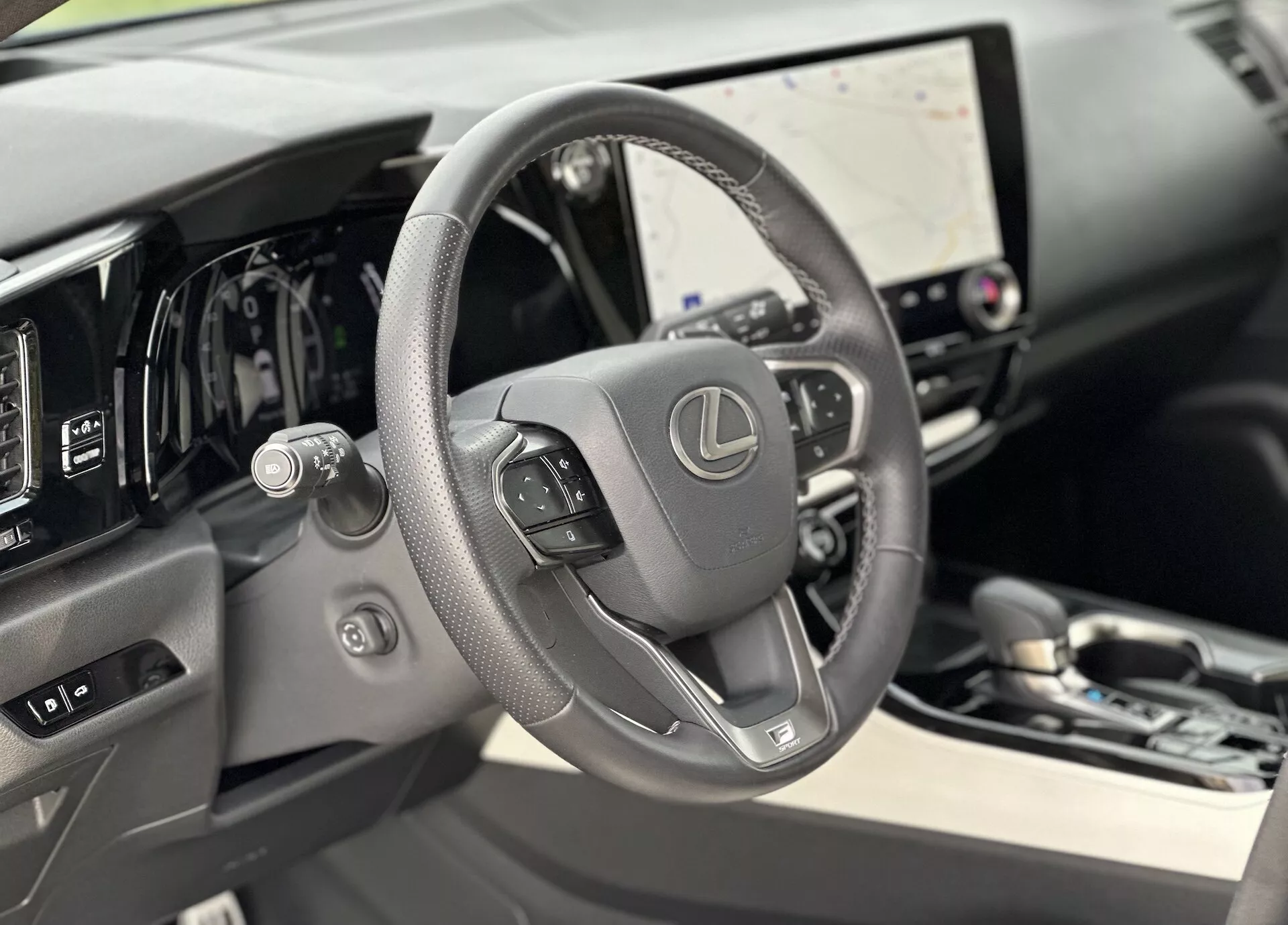 Pogled v notranjost Lexusa NX 2021, osredotočen na usnjen volan z nameščenimi kontrolami in digitalno armaturno ploščo za njim, z velikim zaslonom na dotik za infotainment sistem in subtilnimi namigi luksuza v materialih visoke kakovosti