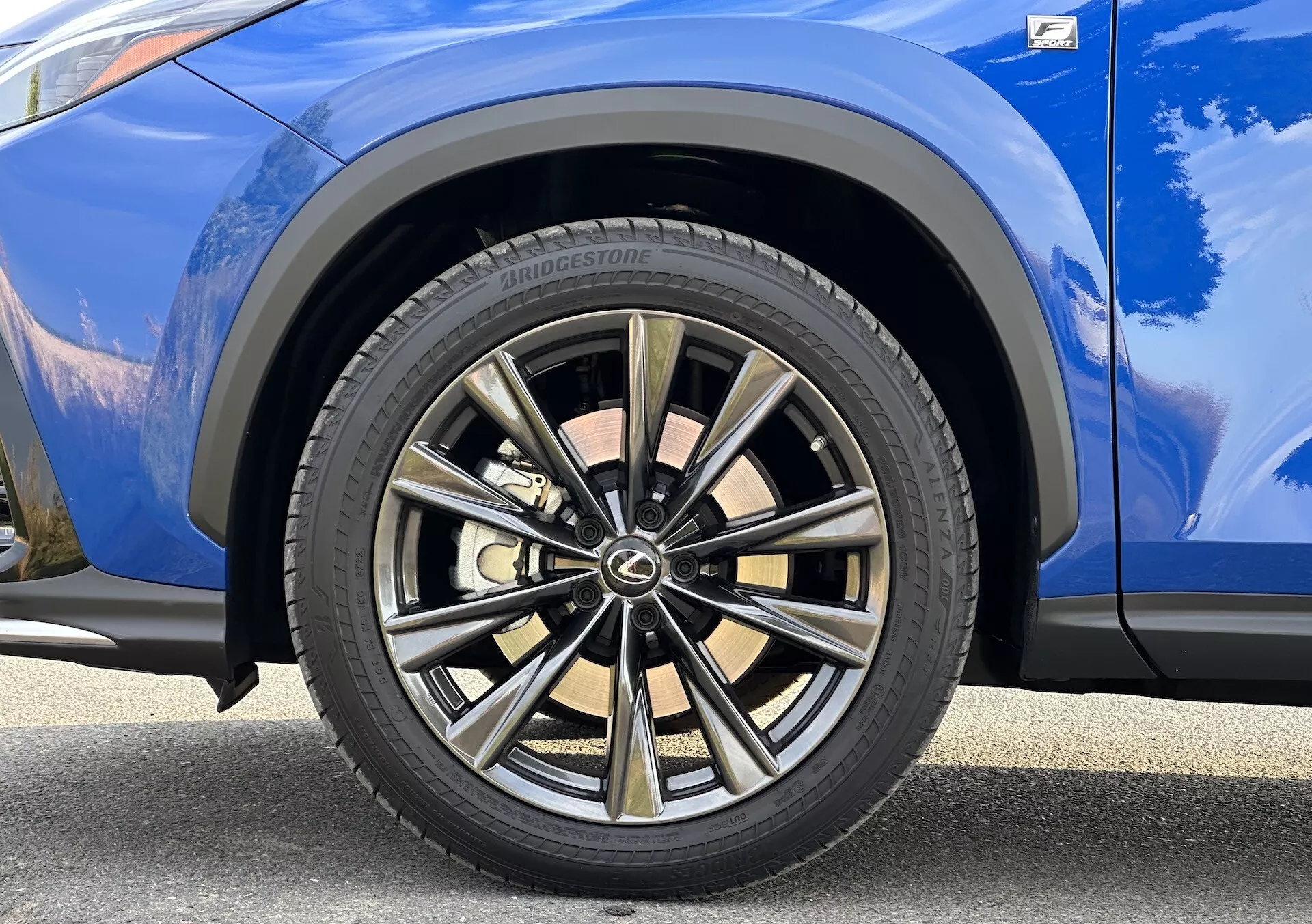 Podroben pogled na sprednje kolo na strani sopotnika Lexus NX 2021 z večkrakim dizajnom z dvobarvno obdelavo in pnevmatiko Bridgestone, ob živahno modrem lakiranem